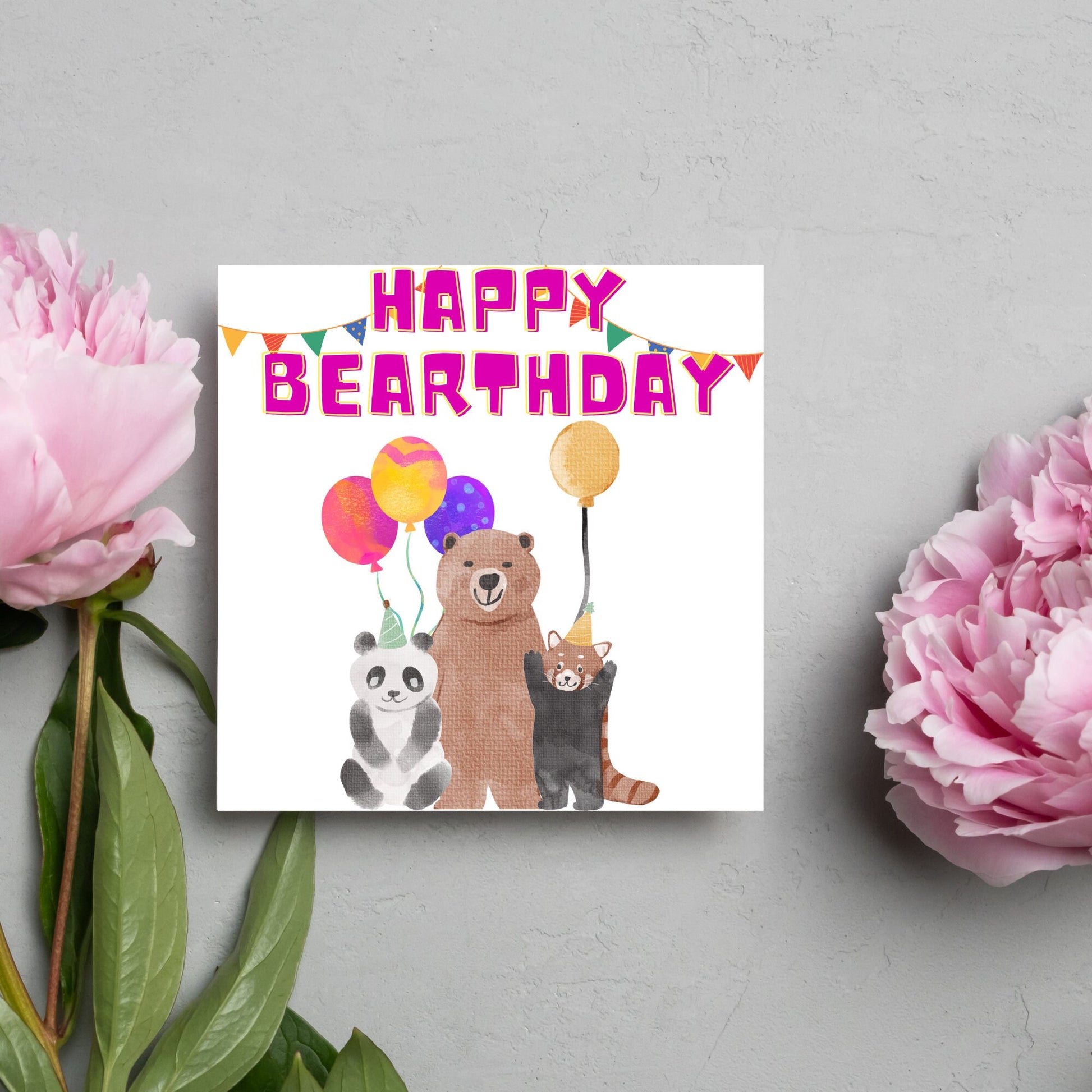 Image of a square Birthday Card. The card has a white background with a vibrant watercolour illustration of 3 bears holding balloons and big pink text that reads happy bearthday, a cute play on the traditional happy birthday.