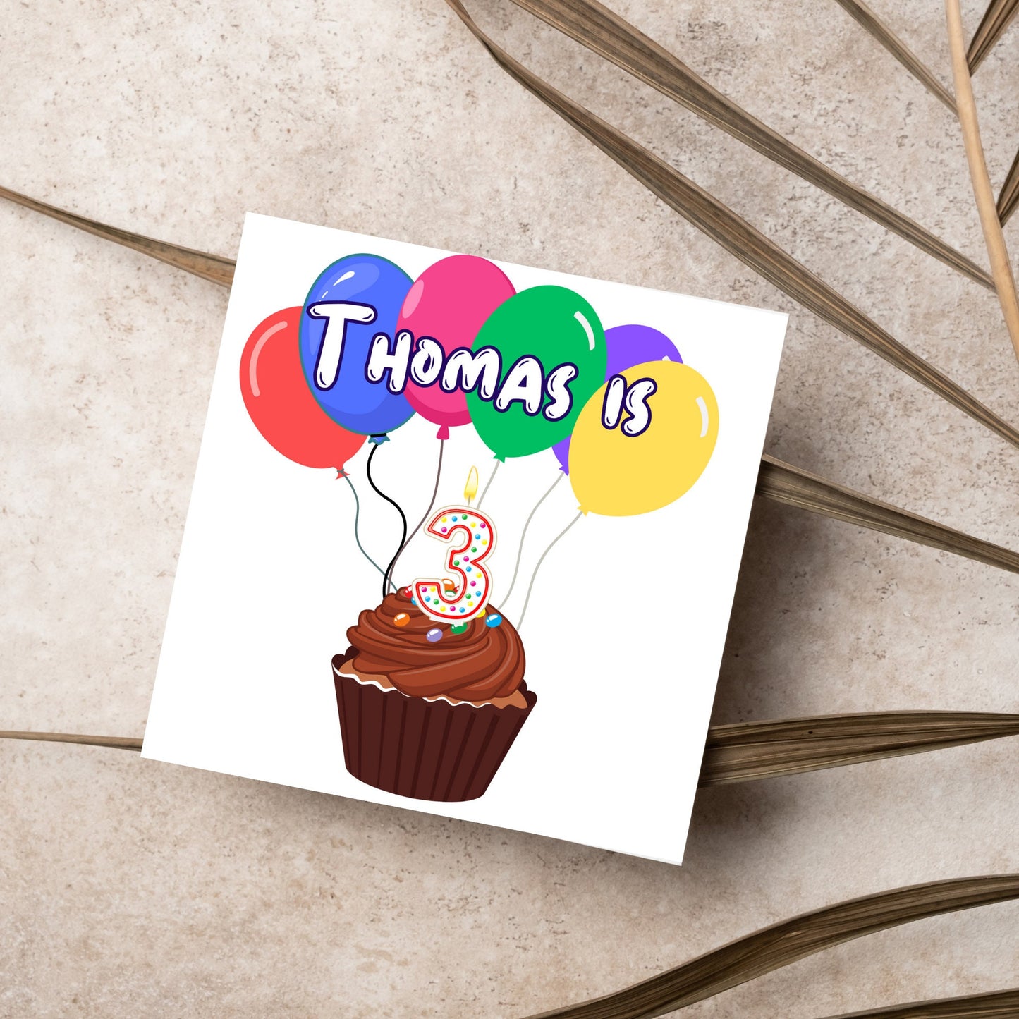 square childs birthday card with chocolate cupcake design personalised with name balloons and a number 3 candle. card reads thomas is 3