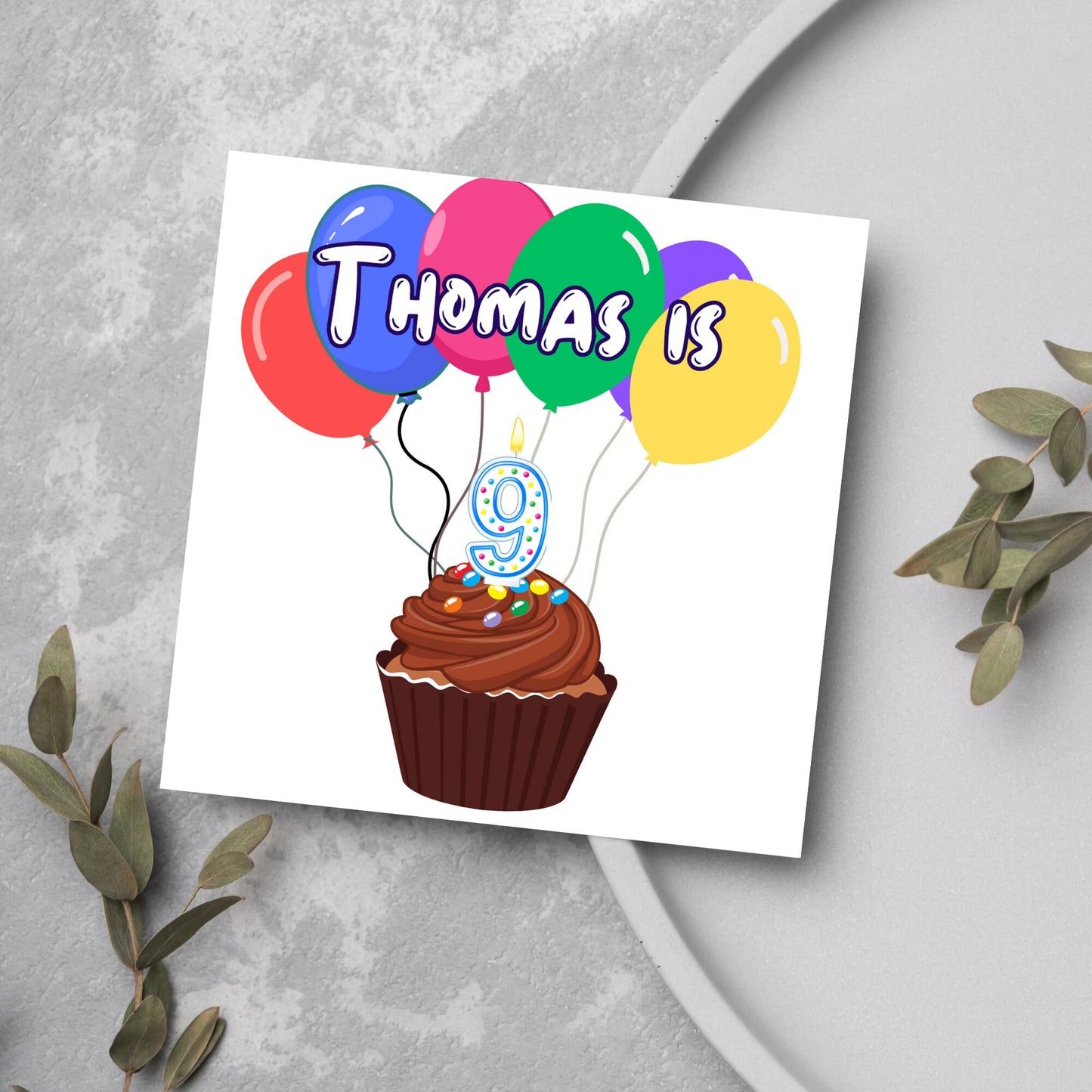 square childs birthday card with chocolate cupcake design personalised with name balloons and a number 9 candle. card reads thomas is 9