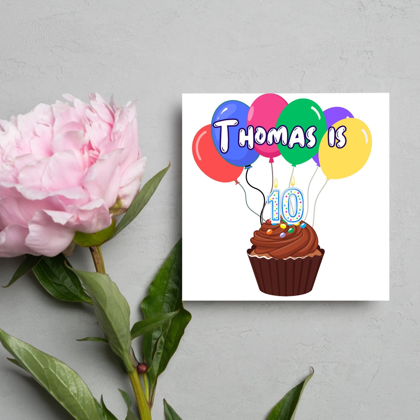 square childs birthday card with chocolate cupcake design personalised with name balloons and a number 10 candle. card reads thomas is 10