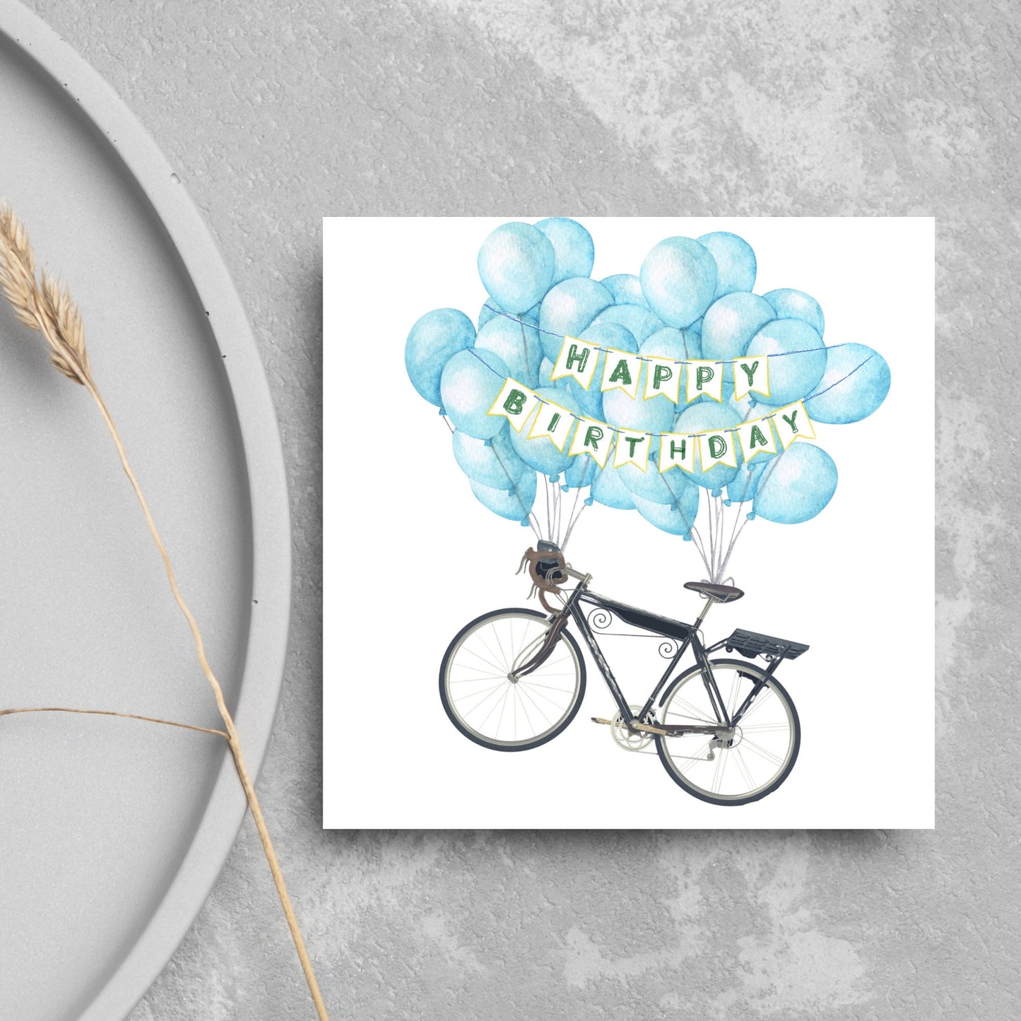 White square birthday card with an illustration of a bicycle being held aloft by blue watercolour balloons and bunting that reads happy birthday