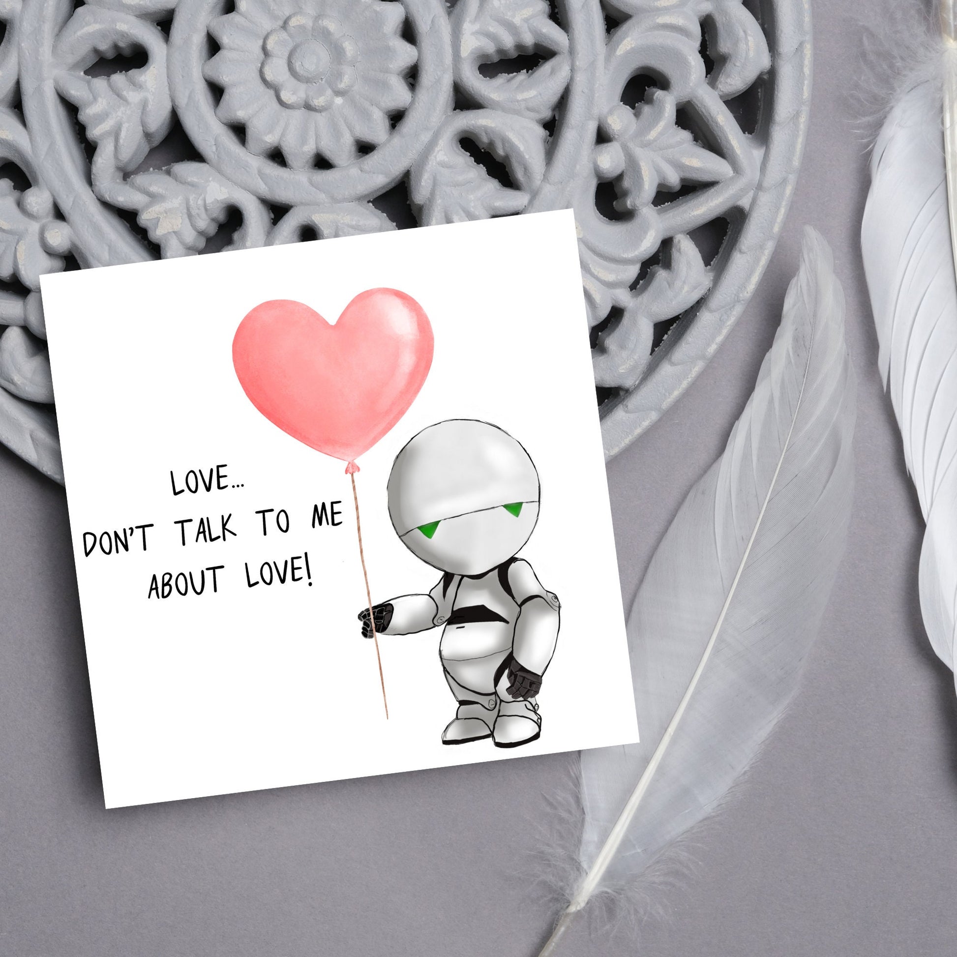 The Square Card has an illistration of Marvin from the classic book, a Hitchhikers guide to the galaxy holding a heart shaped Balloon. It is accompanied by the caption "Love, dont talk to me about Love!"
Funny Love card for boyfriends