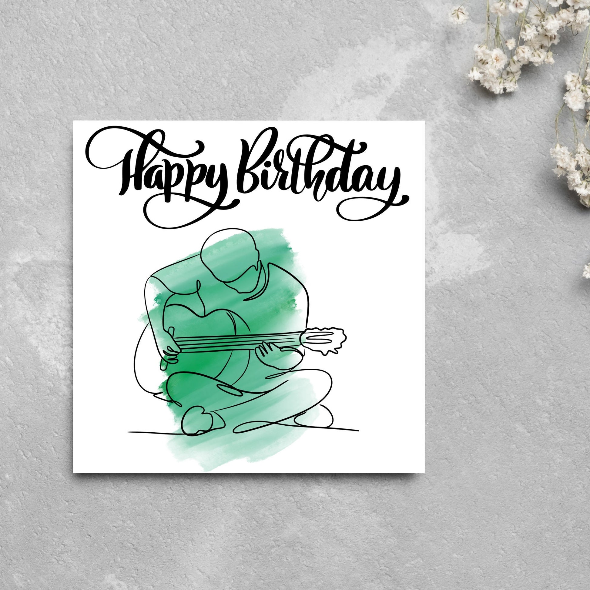 Square birthday card featuring a line drawing of a person sitting cross legged playing a guitar with a green watercolour style backdrop. The top of the card reads Happy Birthday in black swirly writing