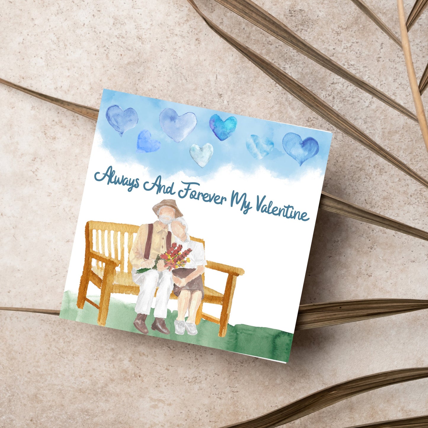 This beautiful Card has a watercolour style print with a couple sitting on a bench with flowers. Above them the blue sky has a series of cute watercolour hearts. This Cute card is perfect for valentines day for your wife or husband