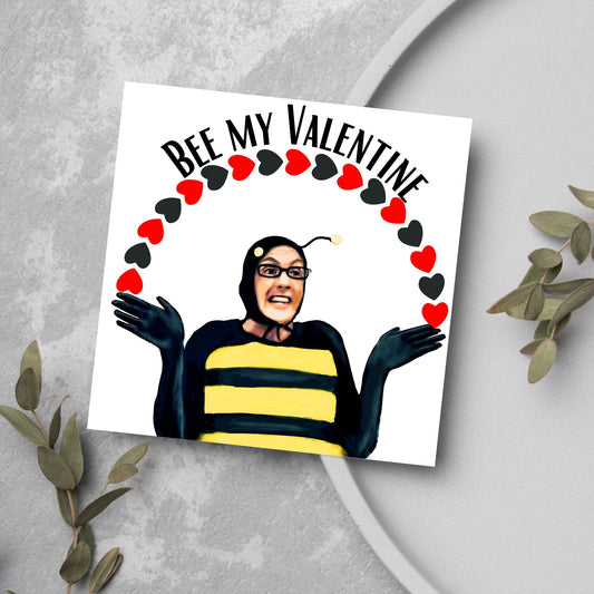 Square greetings card featuring Dean Pelton from the TV show Community, in one of his eccentric costumes dressed as a bee holding an arch of red and black hearts above his head with the text 'Bee my valentine'