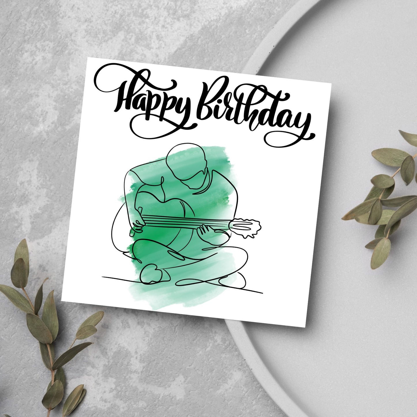 Square birthday card featuring a line drawing of a person sitting cross legged playing a guitar with a green watercolour style backdrop. The top of the card reads Happy Birthday in black swirly writing
