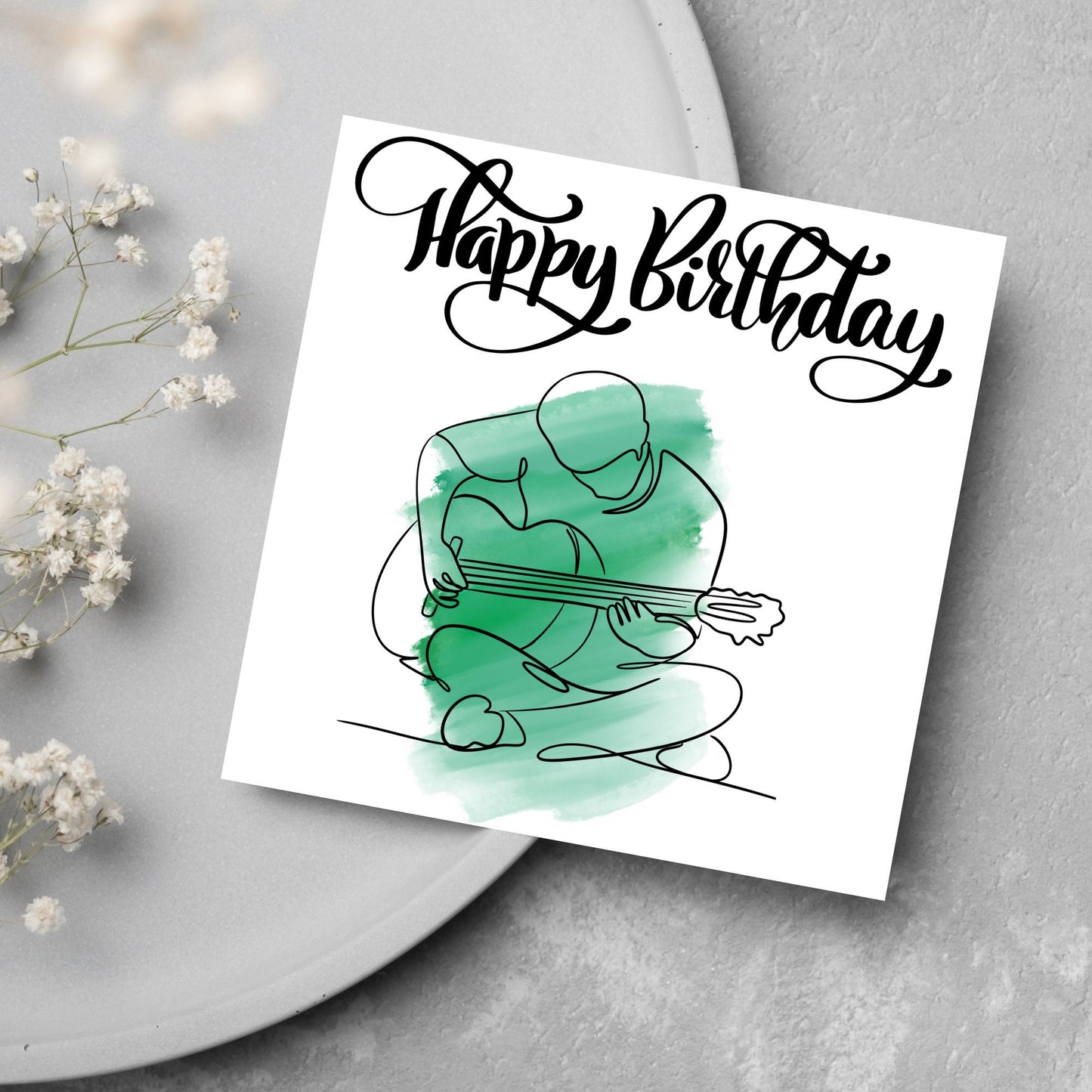 Square birthday card featuring a line drawing of a person sitting cross legged playing a guitar with a green watercolour style backdrop. The top of the card reads Happy Birthday in black swirly writing