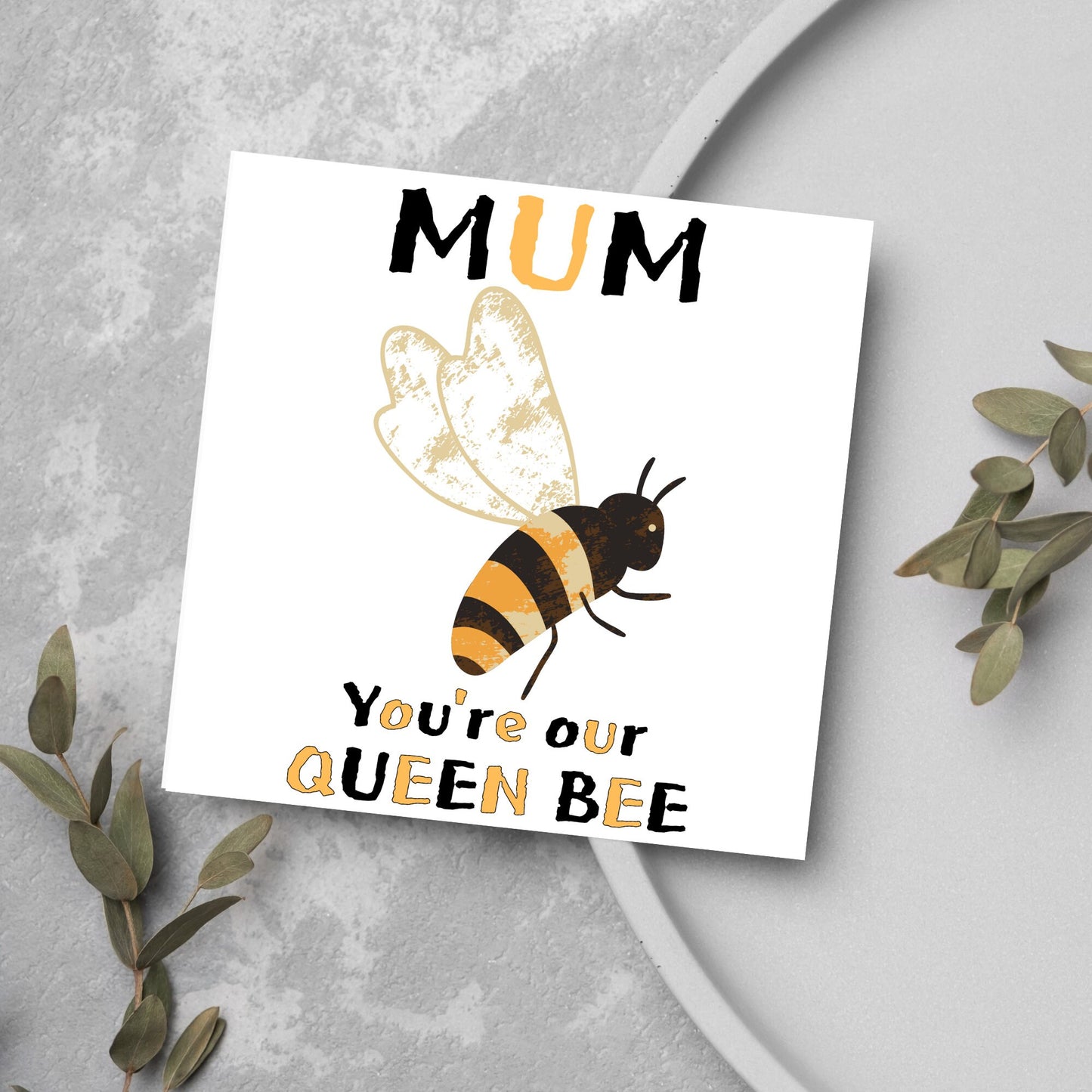 square Birthday card with a watercolour illustration of a bee in the centre and yellow and black text which reads , mum youre our queen bee, in a textured style font resembling pollen