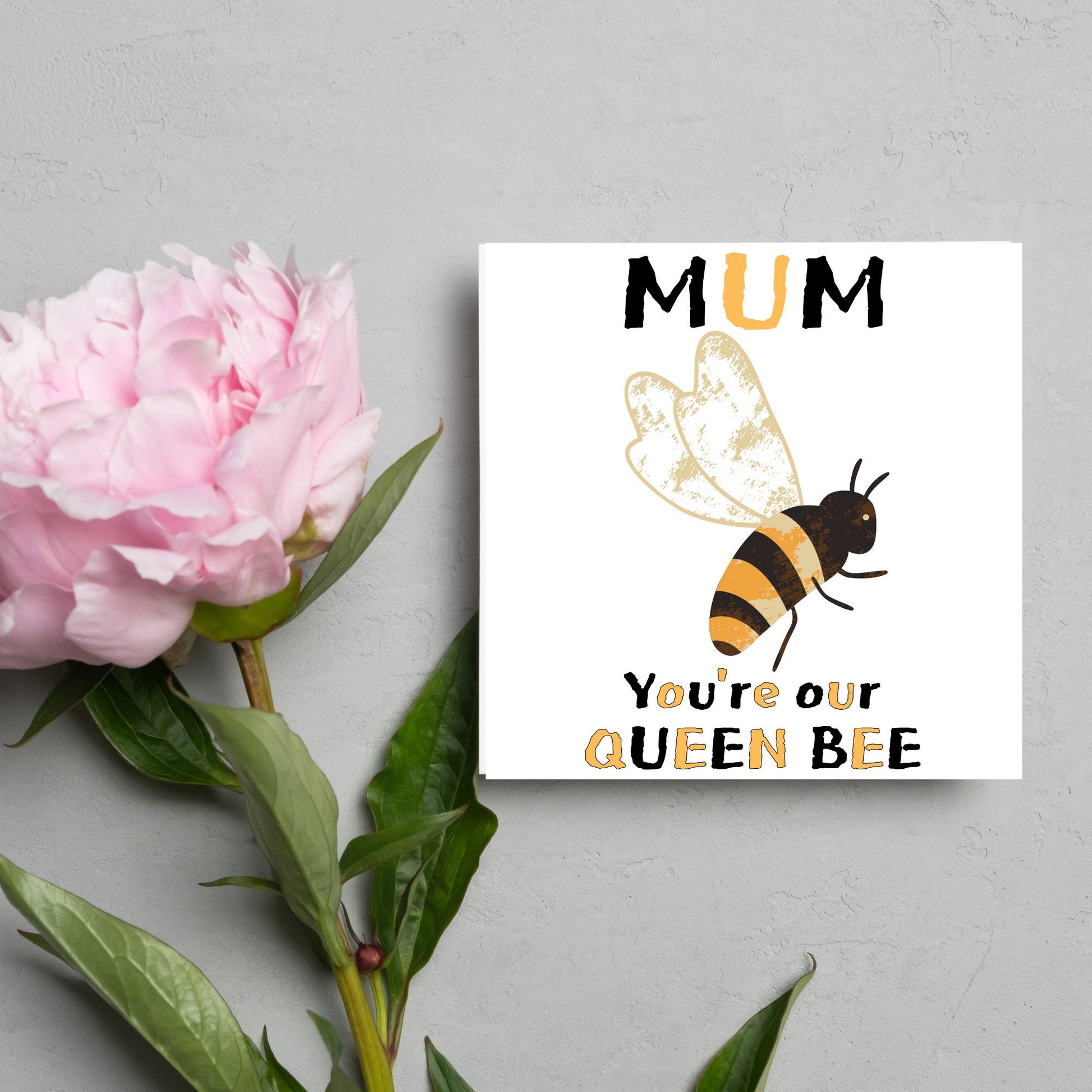 square Birthday card with a watercolour illustration of a bee in the centre and yellow and black text which reads , mum youre our queen bee, in a textured style font resembling pollen