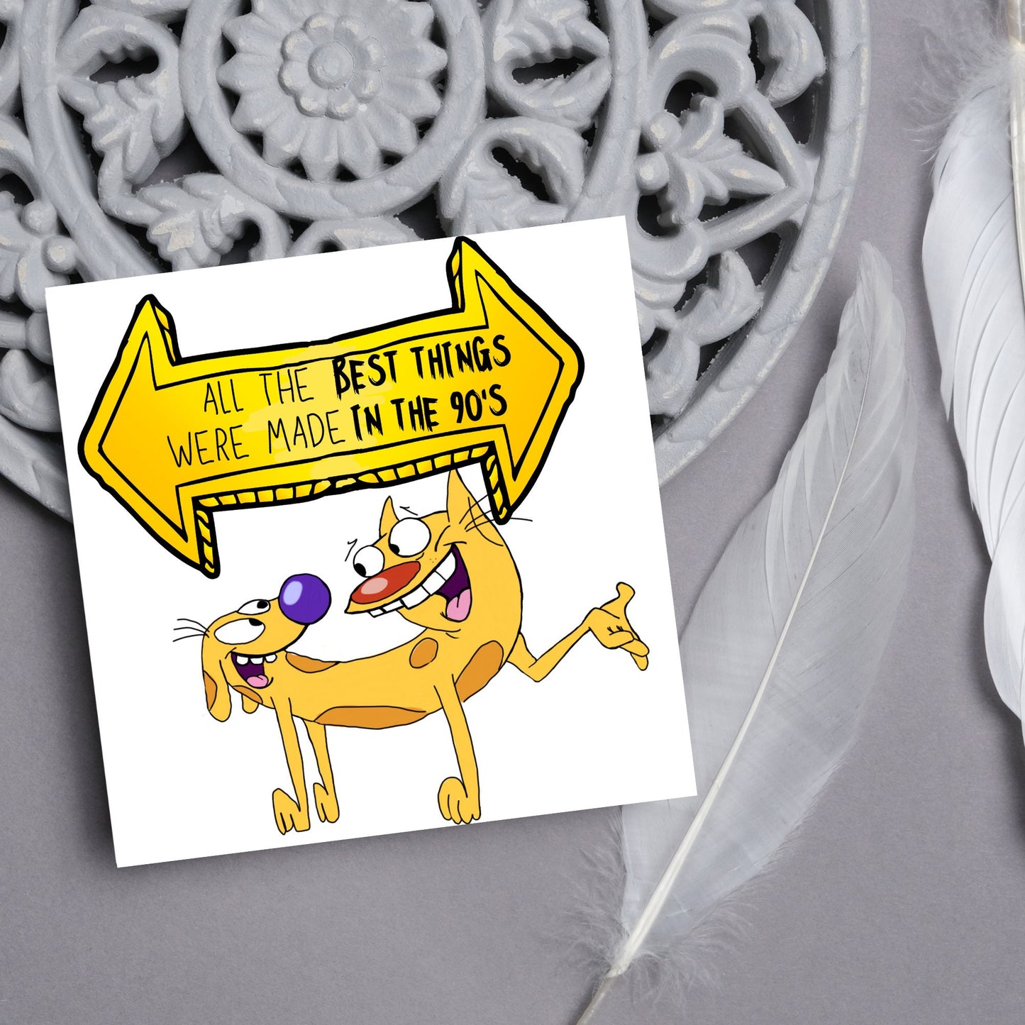square card featuring an illustration of catdog with a yellow and black sign above them with the text that reads 'all the best things were' made in the 90's' in the font from the shows title