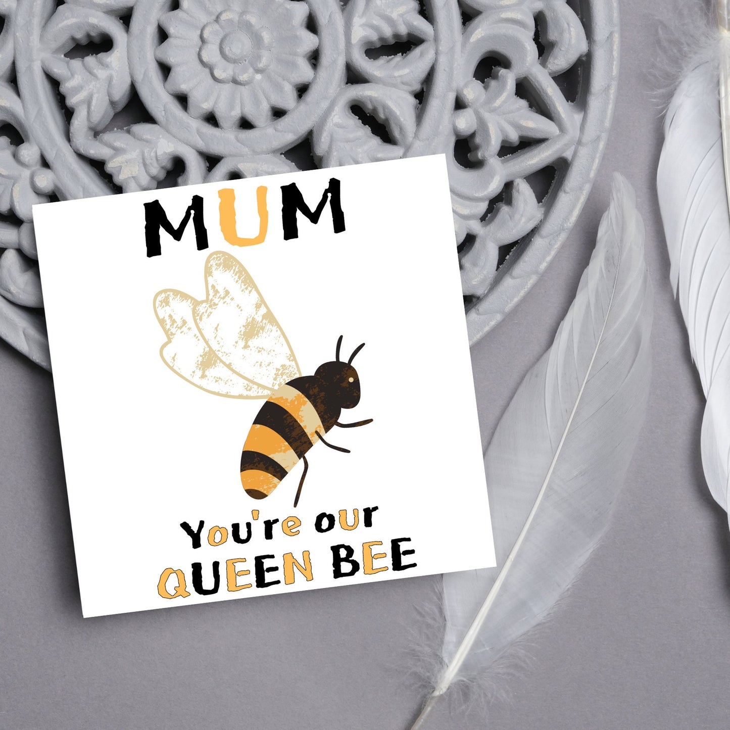 square Birthday card with a watercolour illustration of a bee in the centre and yellow and black text which reads , mum youre our queen bee, in a textured style font resembling pollen