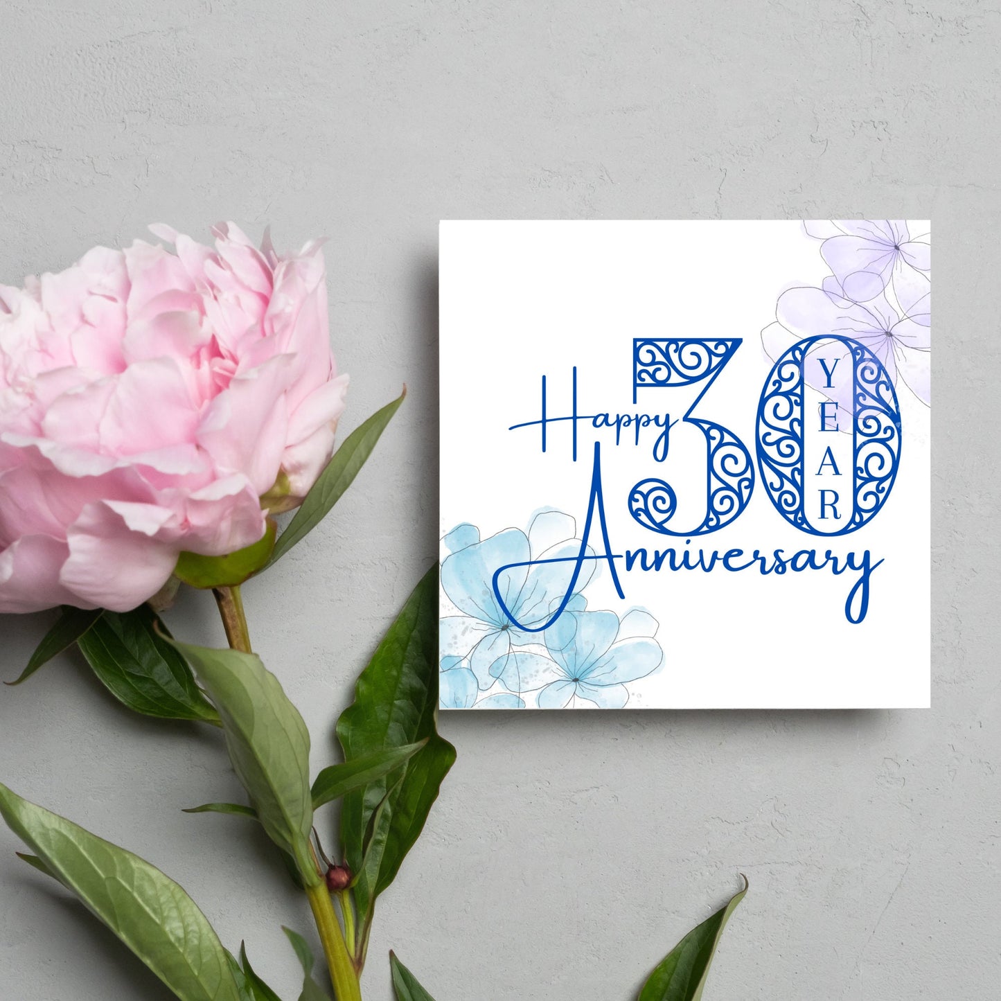 Square Card with white background, there are blue faded watercolour flowers on each corner and dark blue text reads 'Happy 50 year anniversary' the words are in a script font and the number is an ornate filigree style