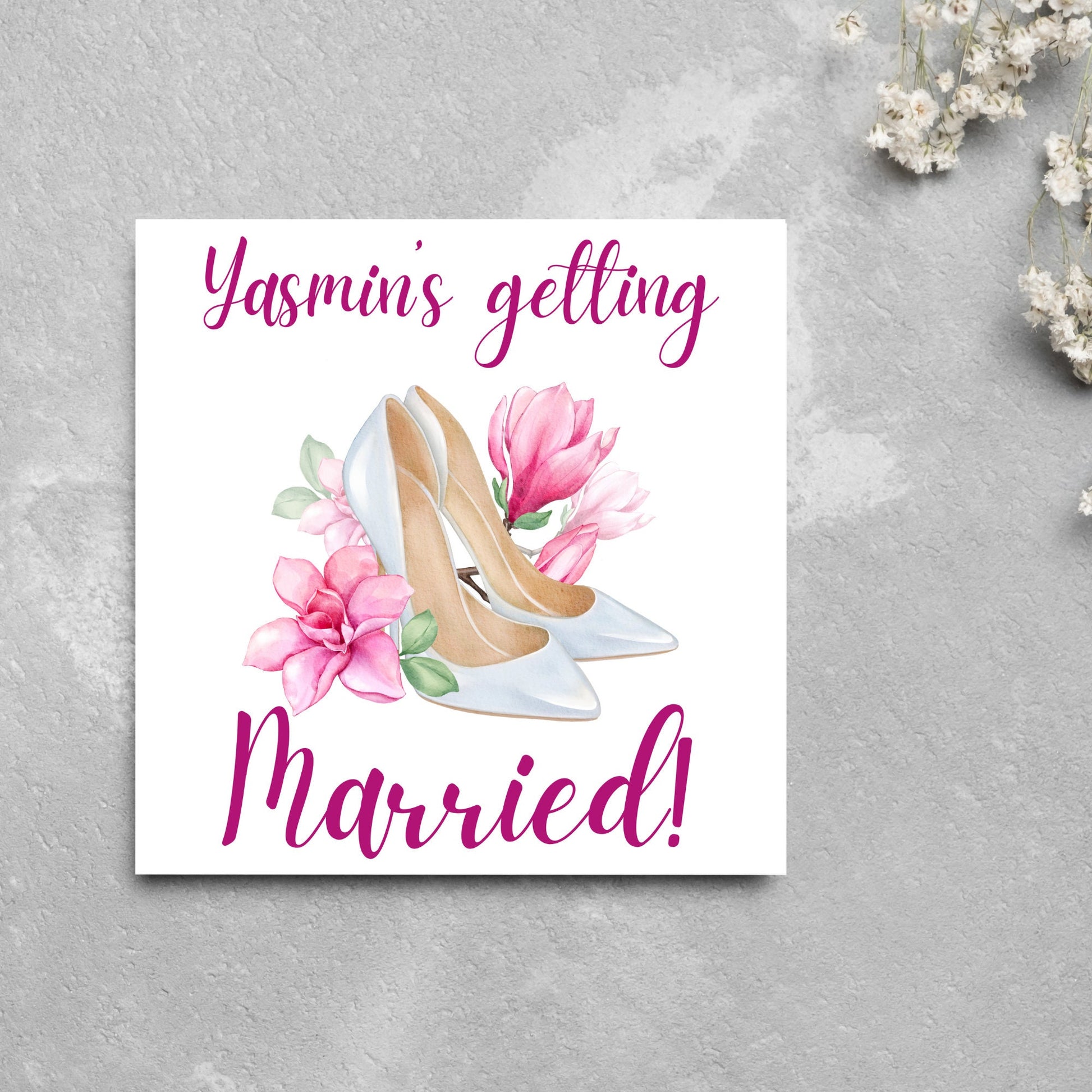 Square card with a watercolour image of white wedding shoes surrounded by pink flowers with pink text that reads Yasmin's getting married in calligraphy style font
