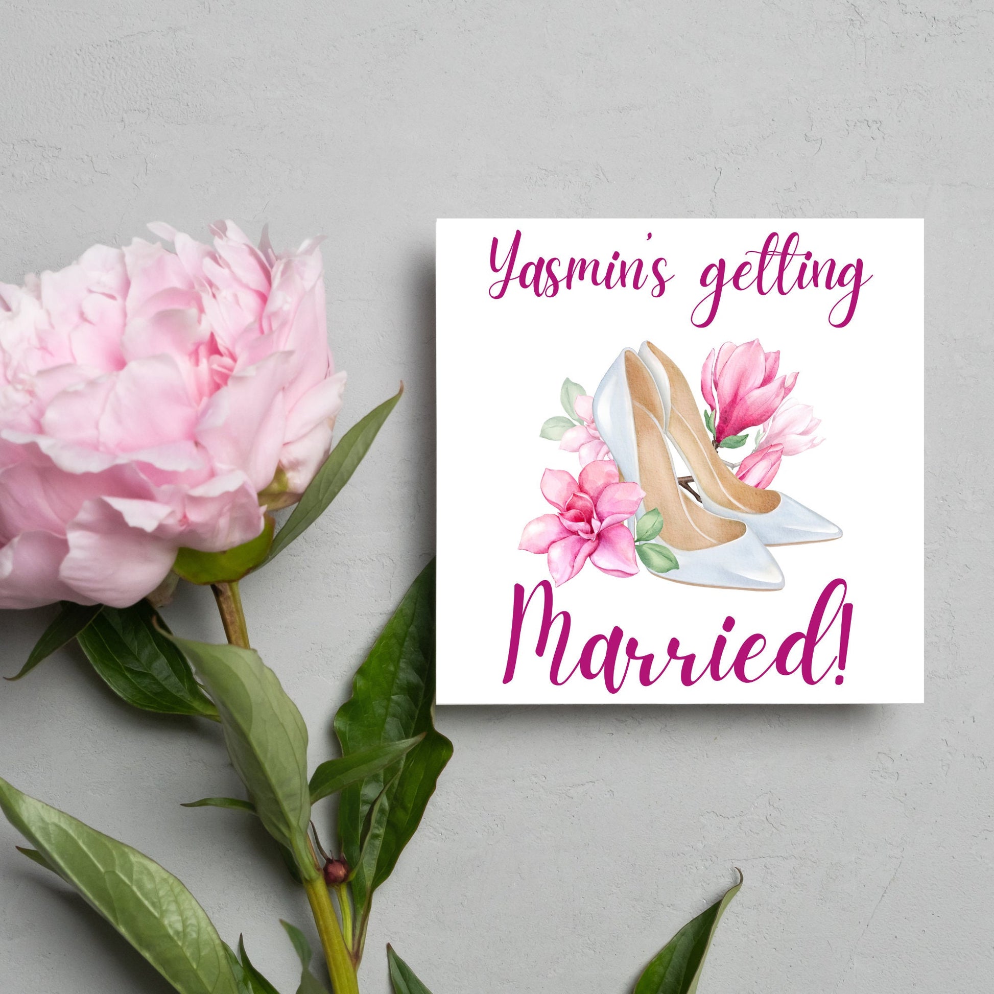 Square card with a watercolour image of white wedding shoes surrounded by pink flowers with pink text that reads Yasmin's getting married in calligraphy style font