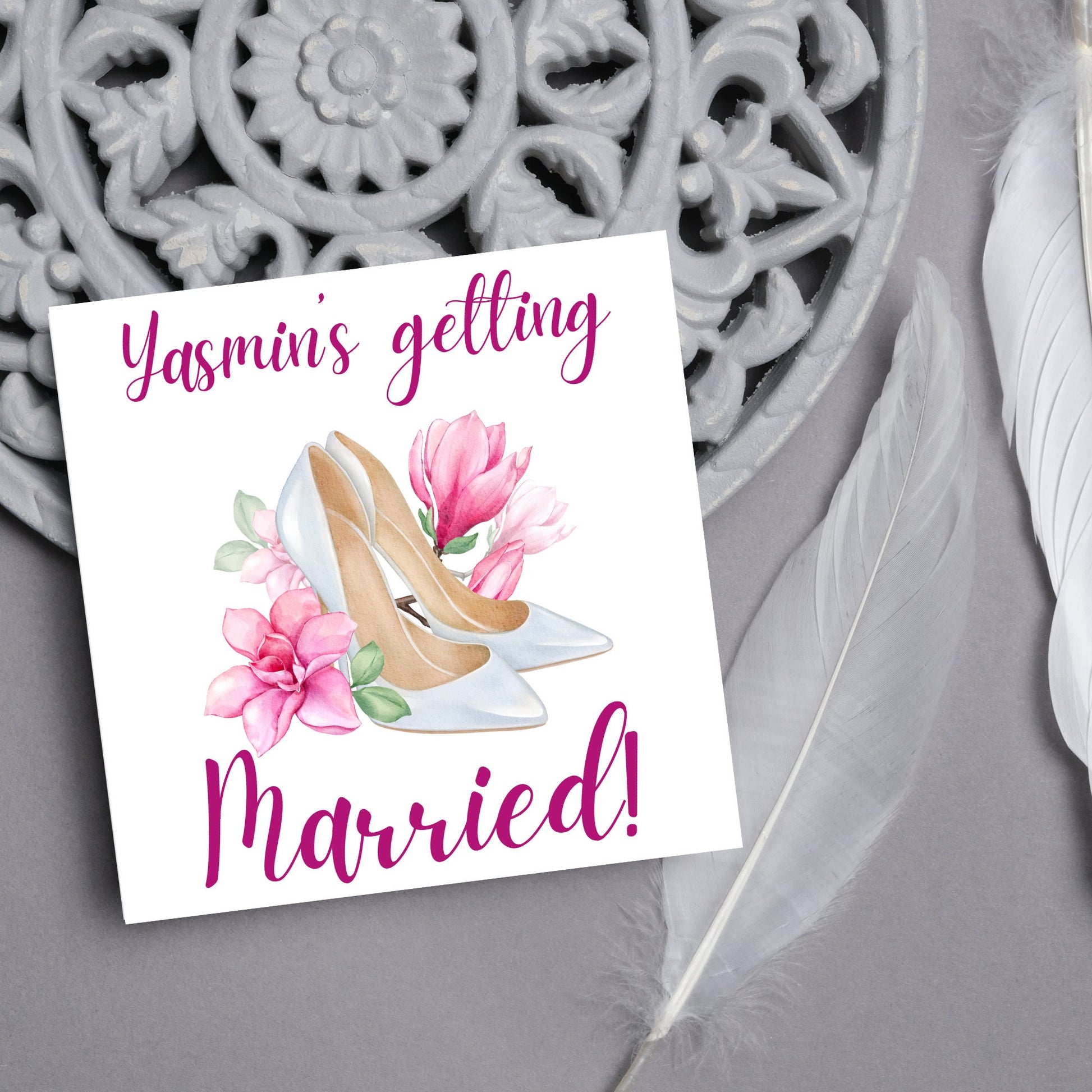 Square card with a watercolour image of white wedding shoes surrounded by pink flowers with pink text that reads Yasmin's getting married in calligraphy style font