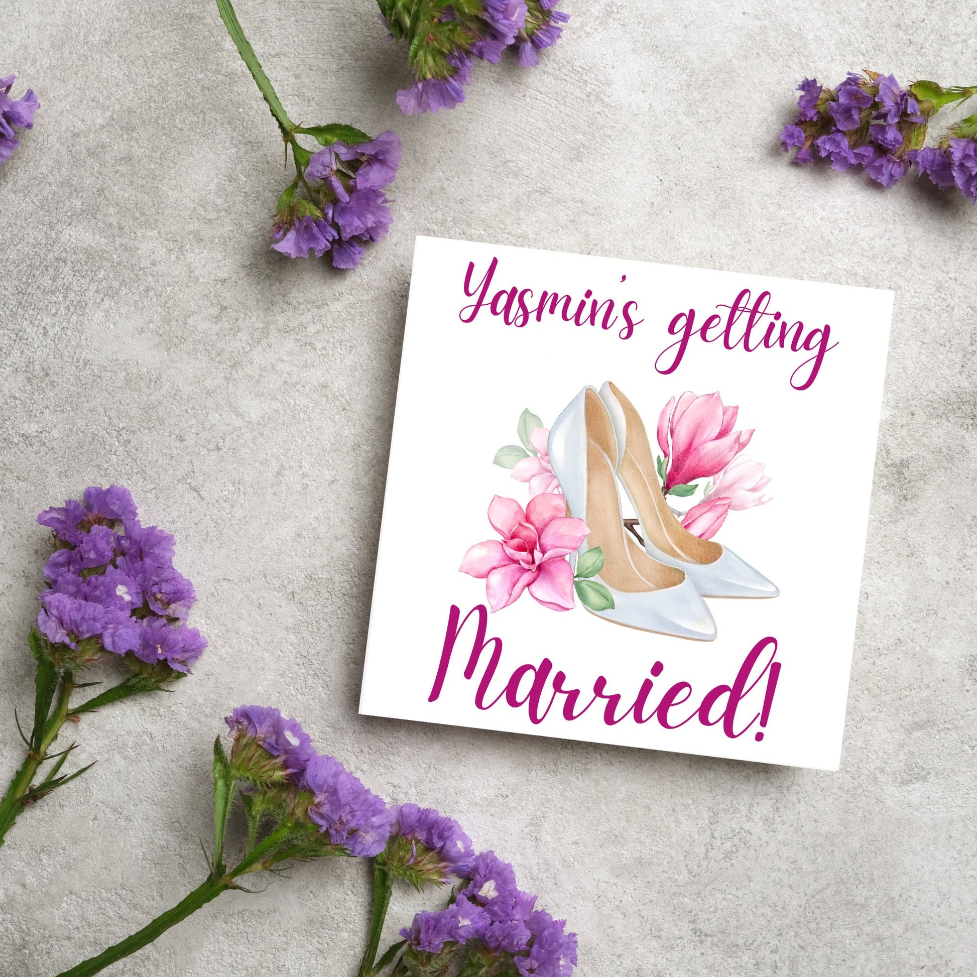 Square card with a watercolour image of white wedding shoes surrounded by pink flowers with pink text that reads Yasmin's getting married in calligraphy style font