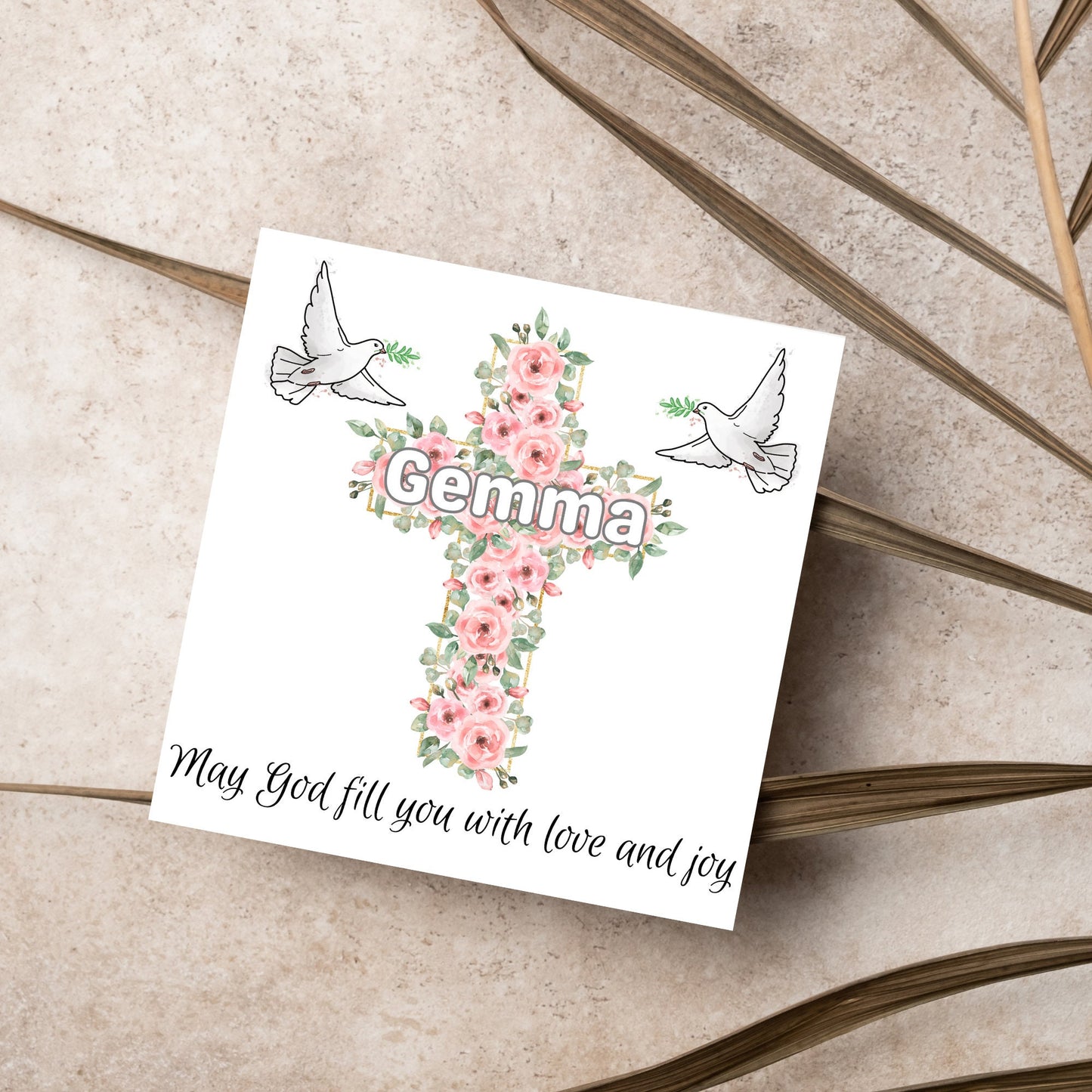 Square white card with a cross made of pink roses at the centre with the chosen name written across in white. either side of the cross is a white dove flying. At the bottom the text 'may god fill you with love and joy' is written