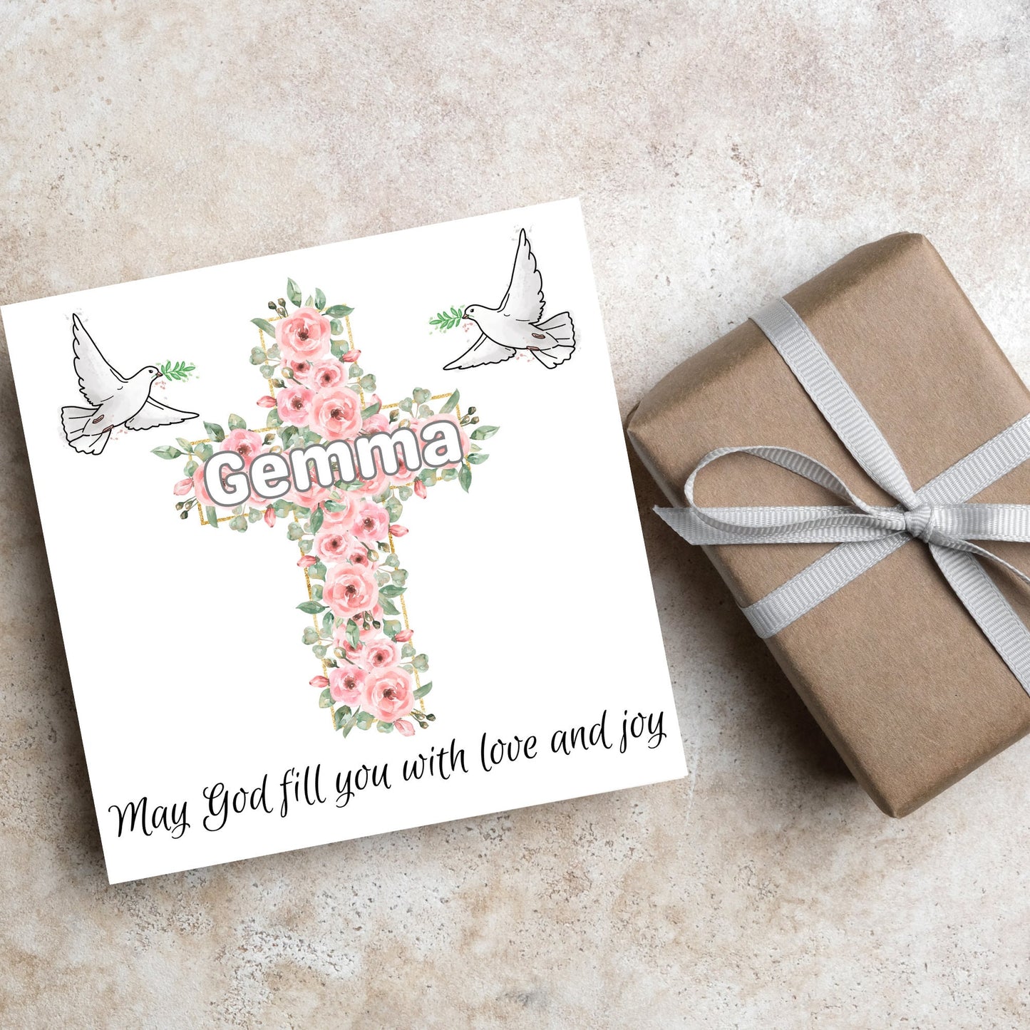 Square white card with a cross made of pink roses at the centre with the chosen name written across in white. either side of the cross is a white dove flying. At the bottom the text 'may god fill you with love and joy' is written