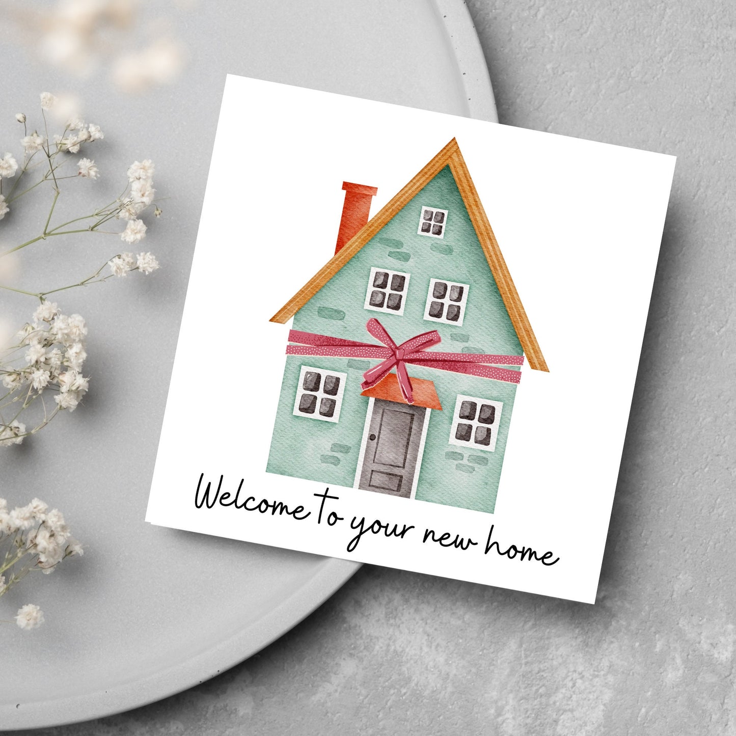 Square card with white background and a watercolour style illlustration of a green three storey house with a red bow wrapped around it. Underneath the house ina script font are the words 'welcome to your new home'