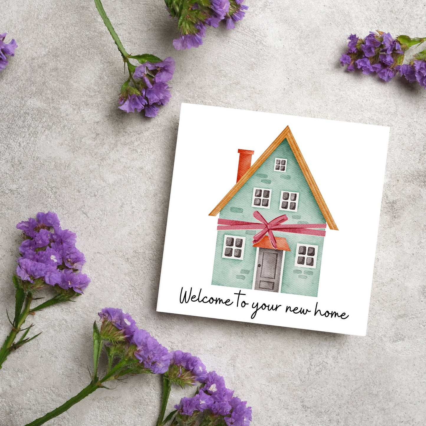 Square card with white background and a watercolour style illlustration of a green three storey house with a red bow wrapped around it. Underneath the house ina script font are the words 'welcome to your new home'
