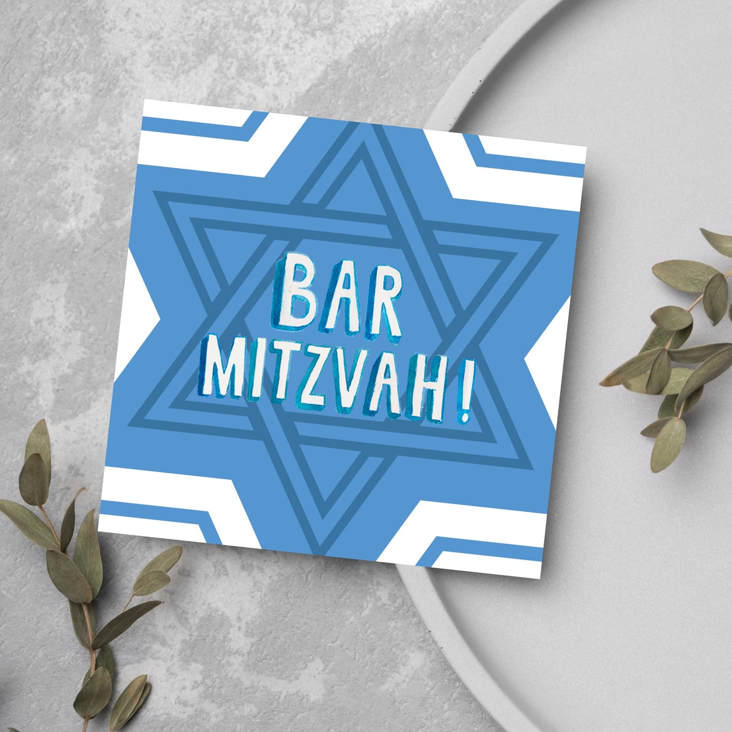 white and blue bar mitzvah card, geometric design with a repeating star of david at the centre in various shades of blue. At the centre of the card in white writing are the words 'bar mitzvah!' in capital letters in a handwritten style font