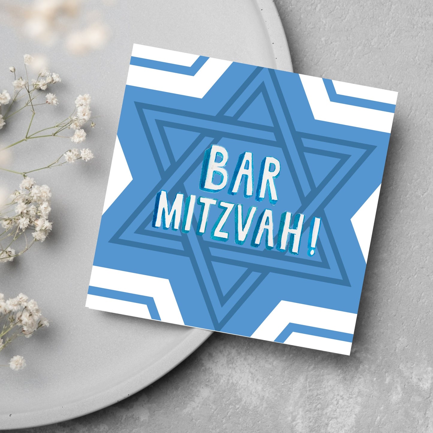 white and blue bar mitzvah card, geometric design with a repeating star of david at the centre in various shades of blue. At the centre of the card in white writing are the words 'bar mitzvah!' in capital letters in a handwritten style font