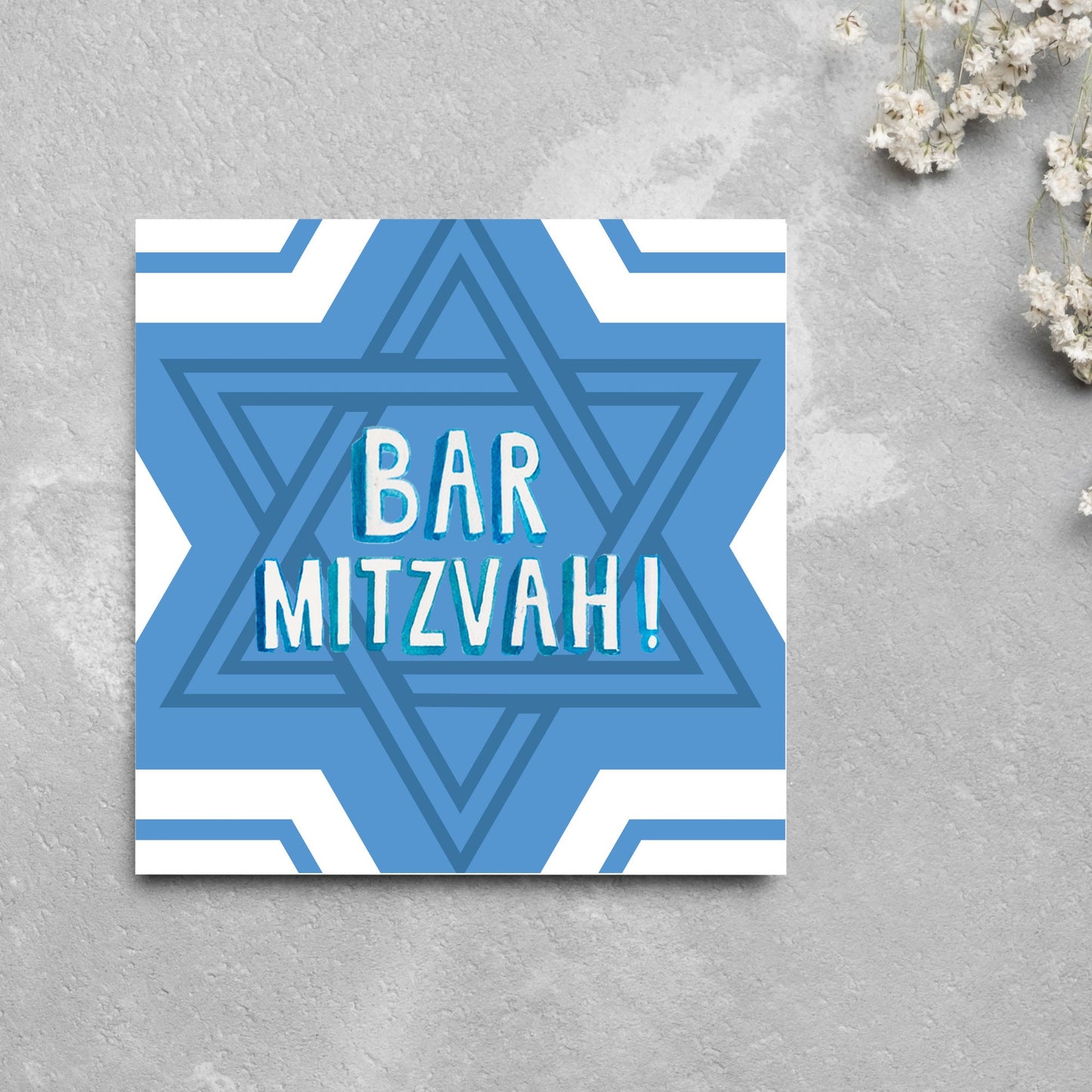 white and blue bar mitzvah card, geometric design with a repeating star of david at the centre in various shades of blue. At the centre of the card in white writing are the words 'bar mitzvah!' in capital letters in a handwritten style font