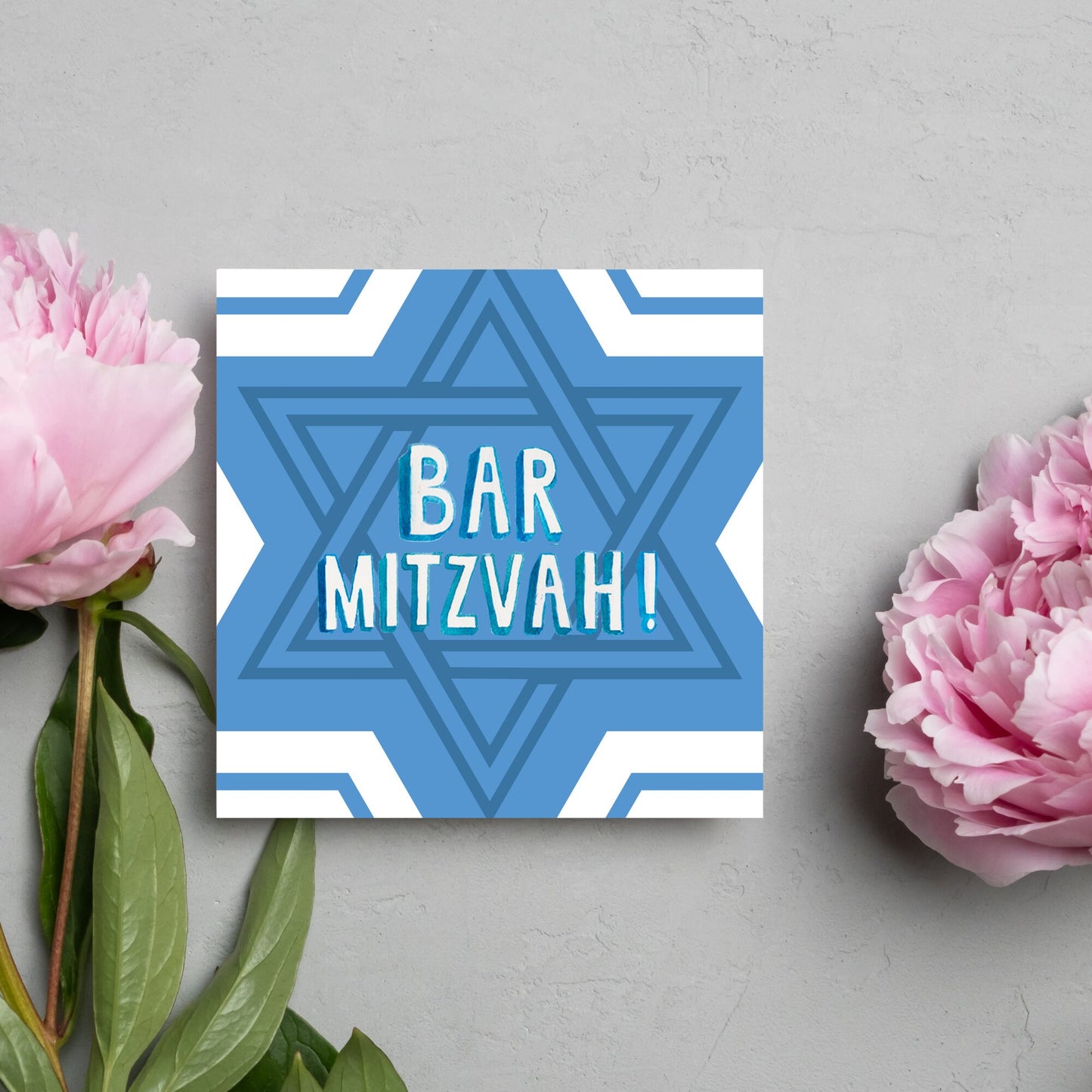 white and blue bar mitzvah card, geometric design with a repeating star of david at the centre in various shades of blue. At the centre of the card in white writing are the words 'bar mitzvah!' in capital letters in a handwritten style font