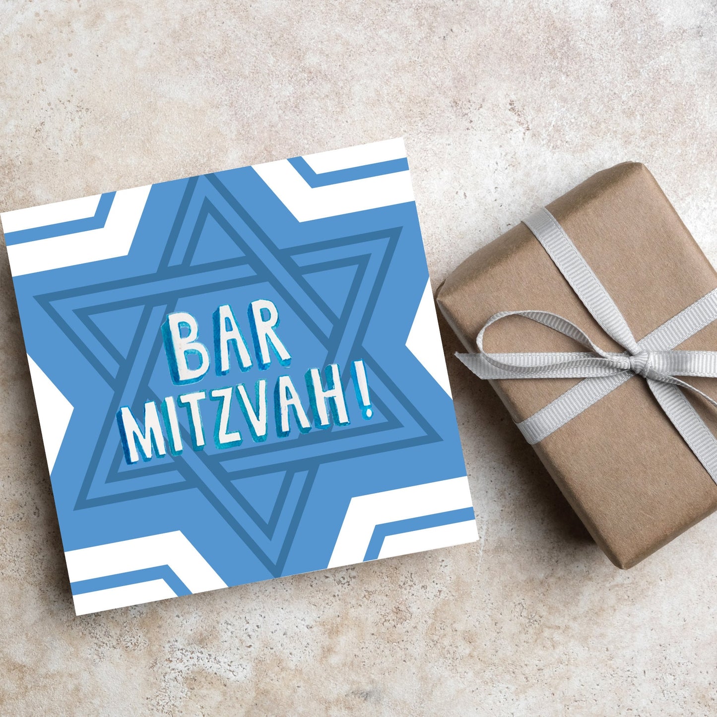 white and blue bar mitzvah card, geometric design with a repeating star of david at the centre in various shades of blue. At the centre of the card in white writing are the words 'bar mitzvah!' in capital letters in a handwritten style font