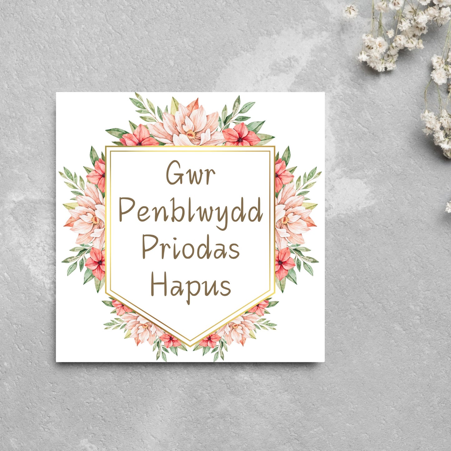 Image of a square wedding anniversary card with 'gwr penblwydd priodas hapus' in a subtle handwritten style font, which translates to 'happy wedding anniversary' in welsh. the text is against a white banner surrounded by pink flowers