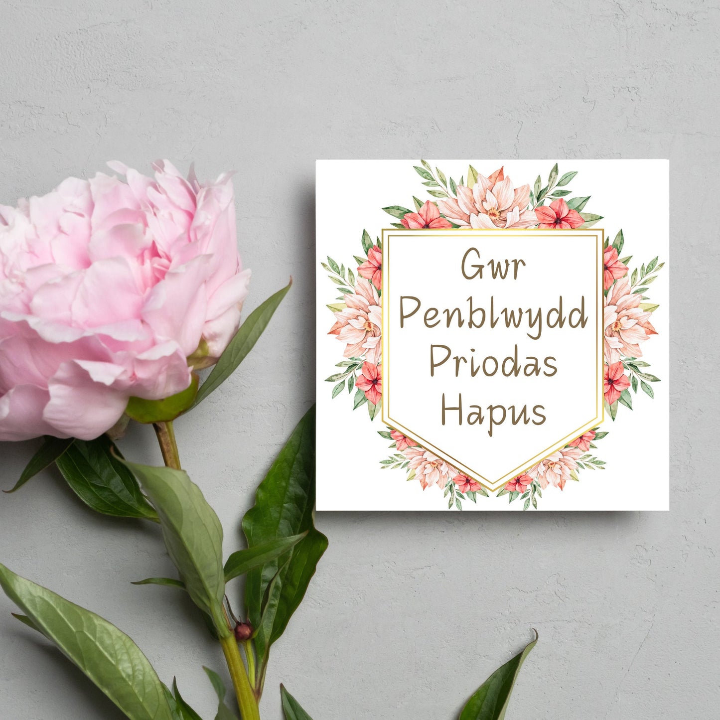 Image of a square wedding anniversary card with 'gwr penblwydd priodas hapus' in a subtle handwritten style font, which translates to 'happy wedding anniversary' in welsh. the text is against a white banner surrounded by pink flowers
