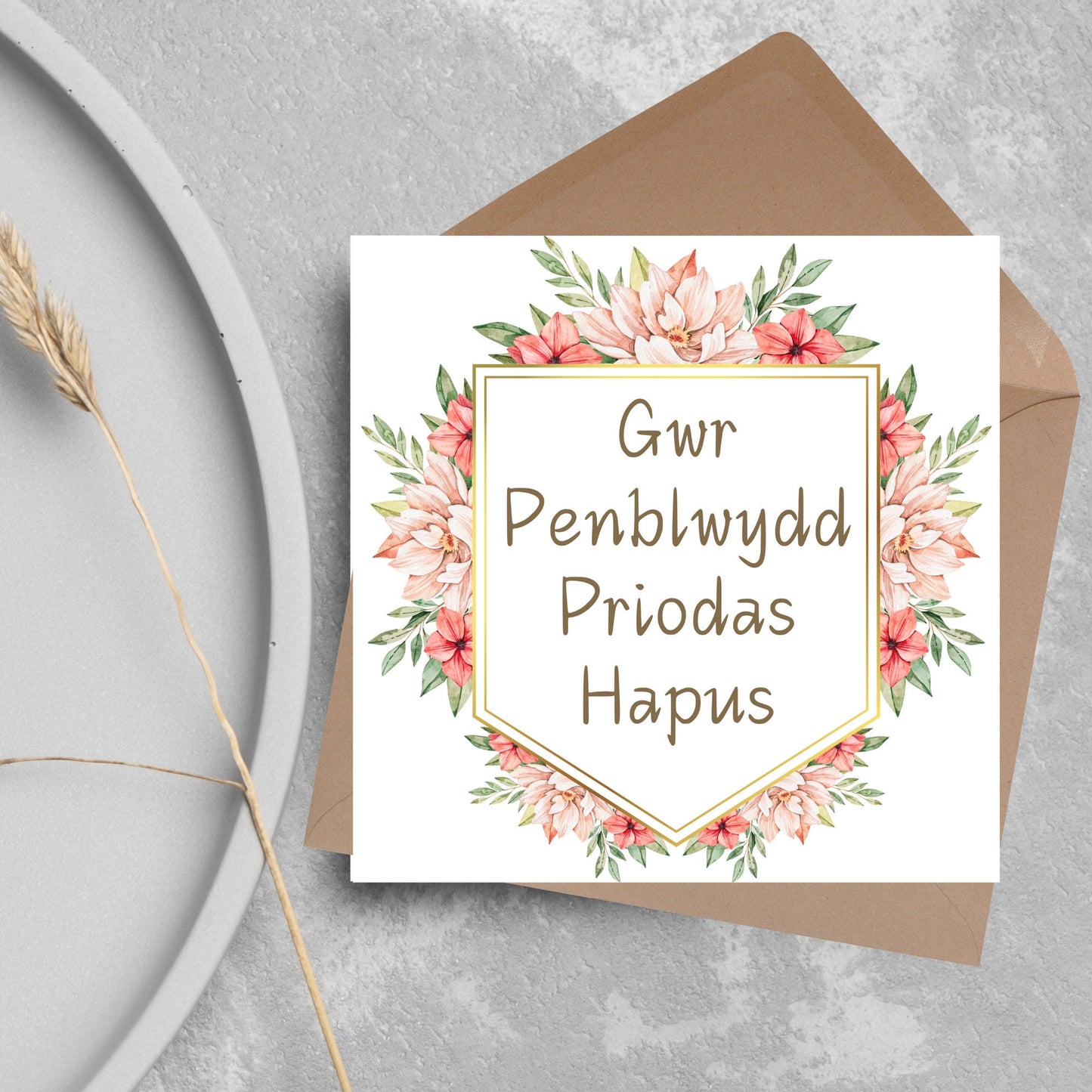 Image of a square wedding anniversary card with 'gwr penblwydd priodas hapus' in a subtle handwritten style font, which translates to 'happy wedding anniversary' in welsh. the text is against a white banner surrounded by pink flowers