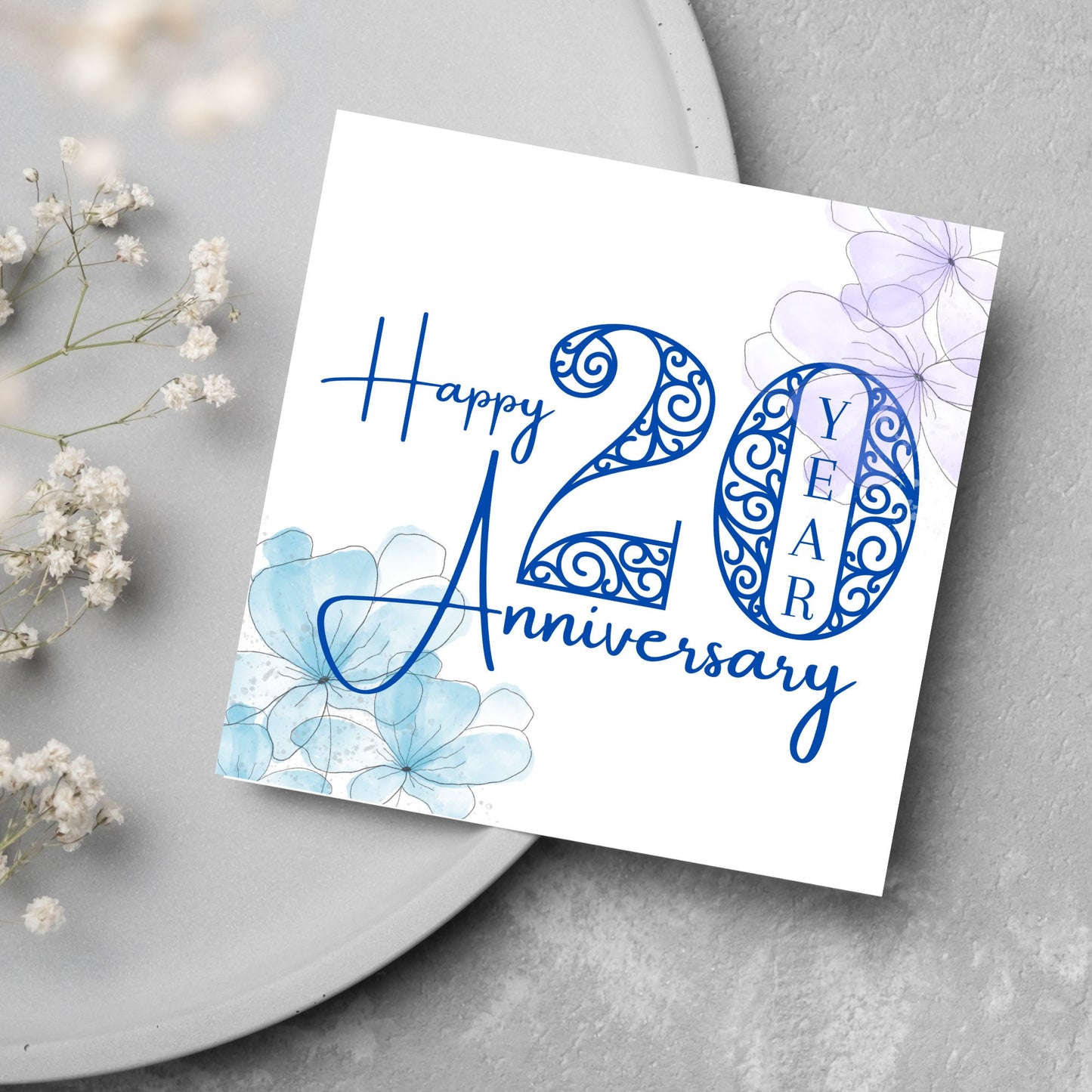 Square Card with white background, there are blue faded watercolour flowers on each corner and dark blue text reads 'Happy 20 year anniversary' the words are in a script font and the number is an ornate filigree style