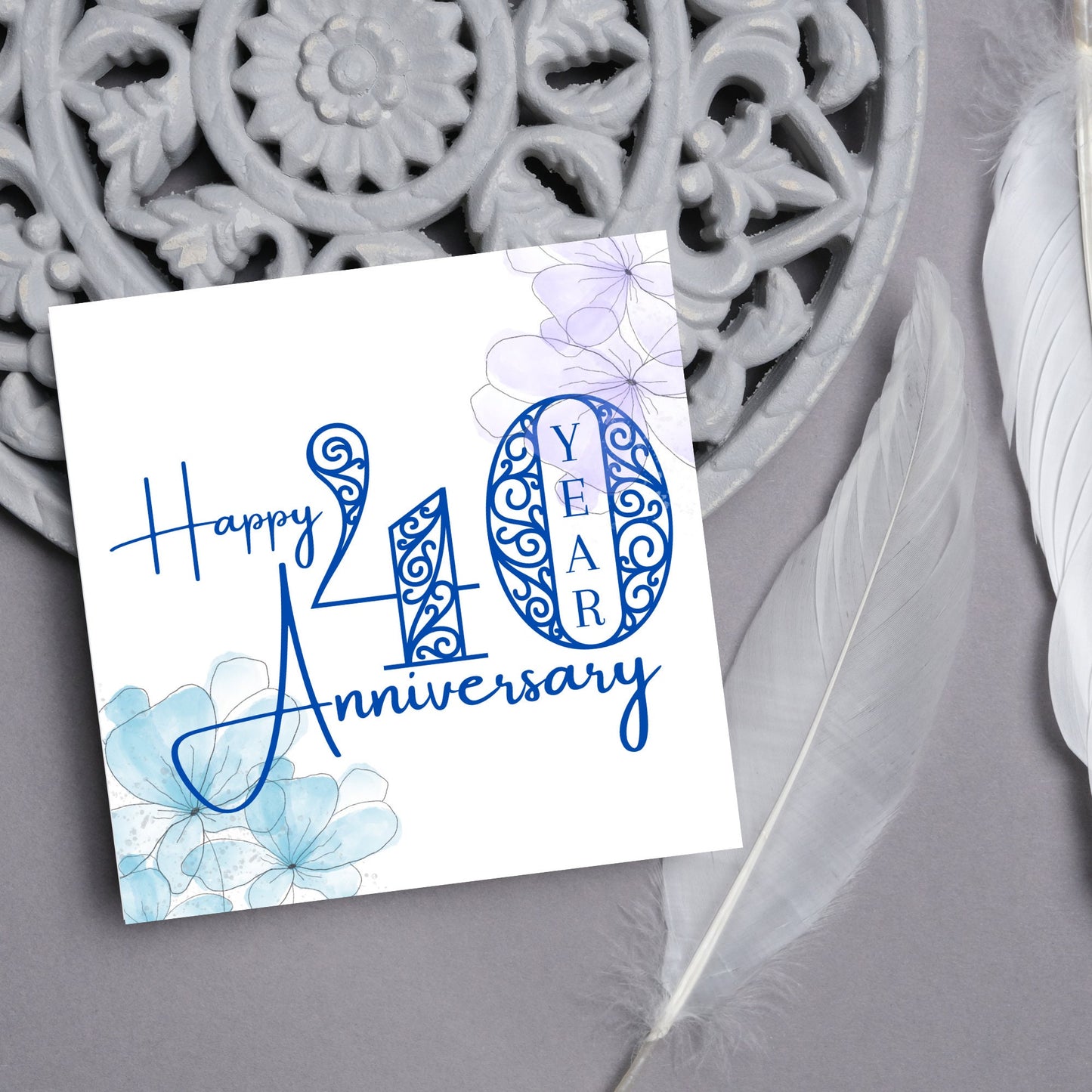 Square Card with white background, there are blue faded watercolour flowers on each corner and dark blue text reads 'Happy 40 year anniversary' the words are in a script font and the number is an ornate filigree style