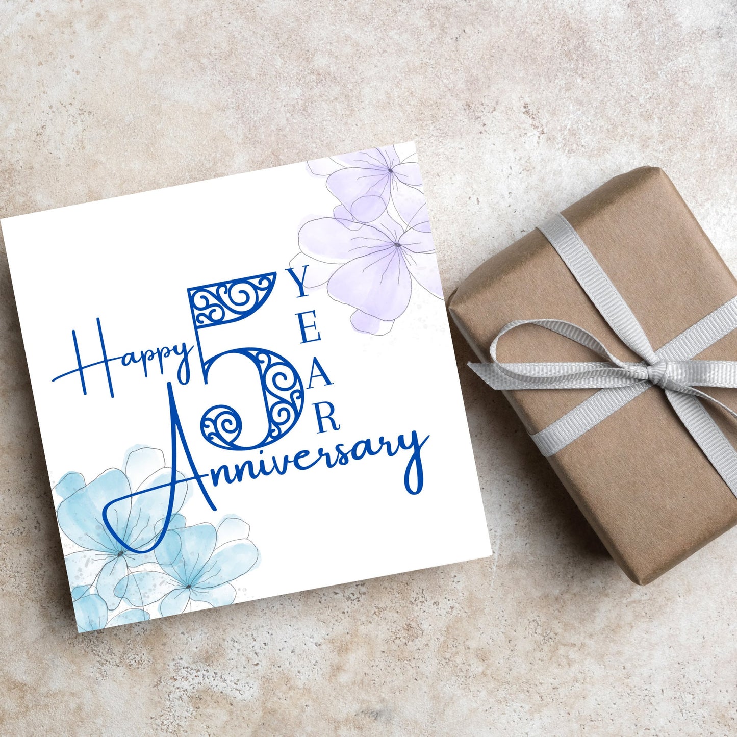 Square Card with white background, there are blue faded watercolour flowers on each corner and dark blue text reads 'Happy 5 year anniversary' the words are in a script font and the number is an ornate filigree style