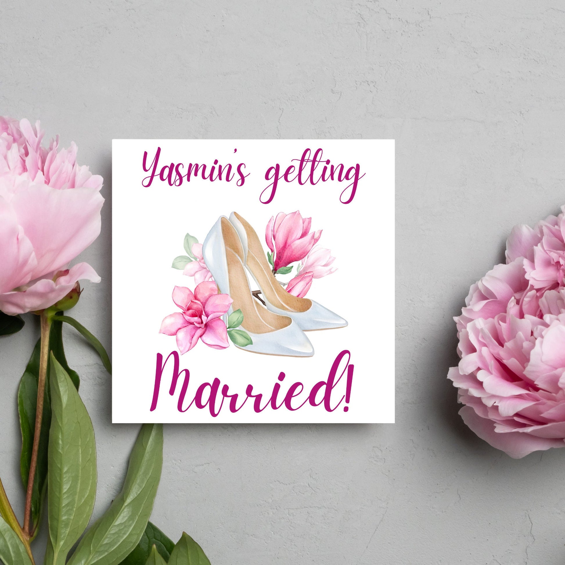 Square card with a watercolour image of white wedding shoes surrounded by pink flowers with pink text that reads Yasmin's getting married in calligraphy style font