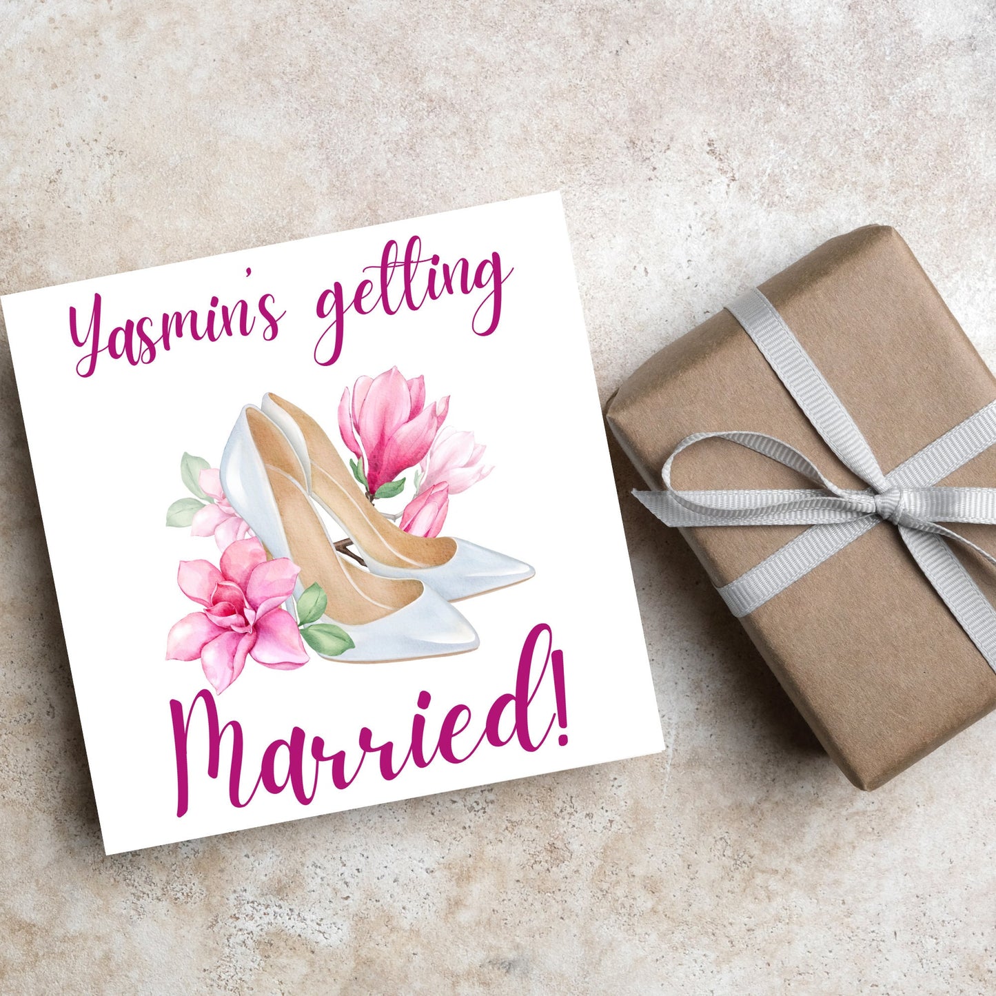 Square card with a watercolour image of white wedding shoes surrounded by pink flowers with pink text that reads Yasmin's getting married in calligraphy style font