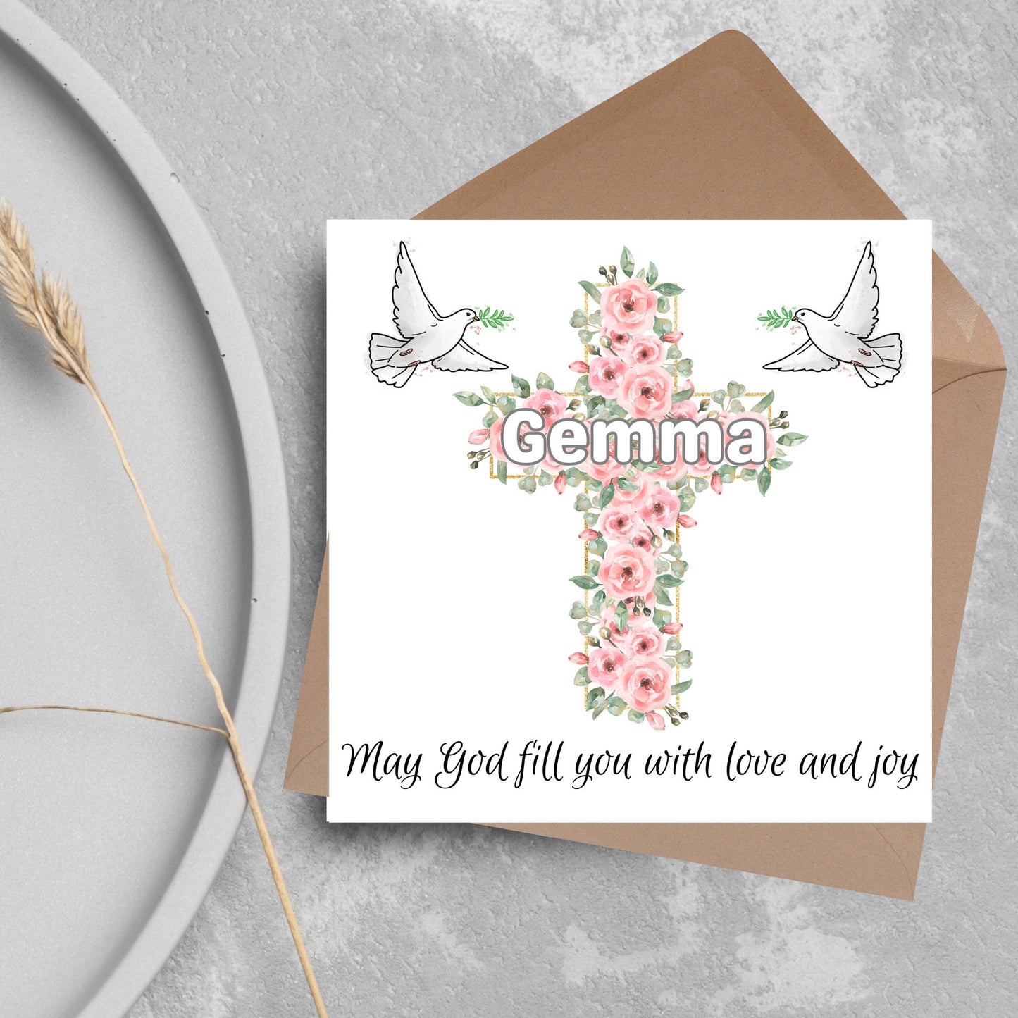 Square white card with a cross made of pink roses at the centre with the chosen name written across in white. either side of the cross is a white dove flying. At the bottom the text 'may god fill you with love and joy' is written