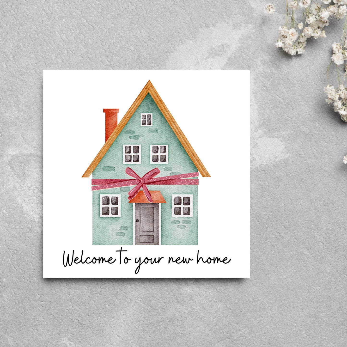 Square card with white background and a watercolour style illlustration of a green three storey house with a red bow wrapped around it. Underneath the house ina script font are the words 'welcome to your new home'