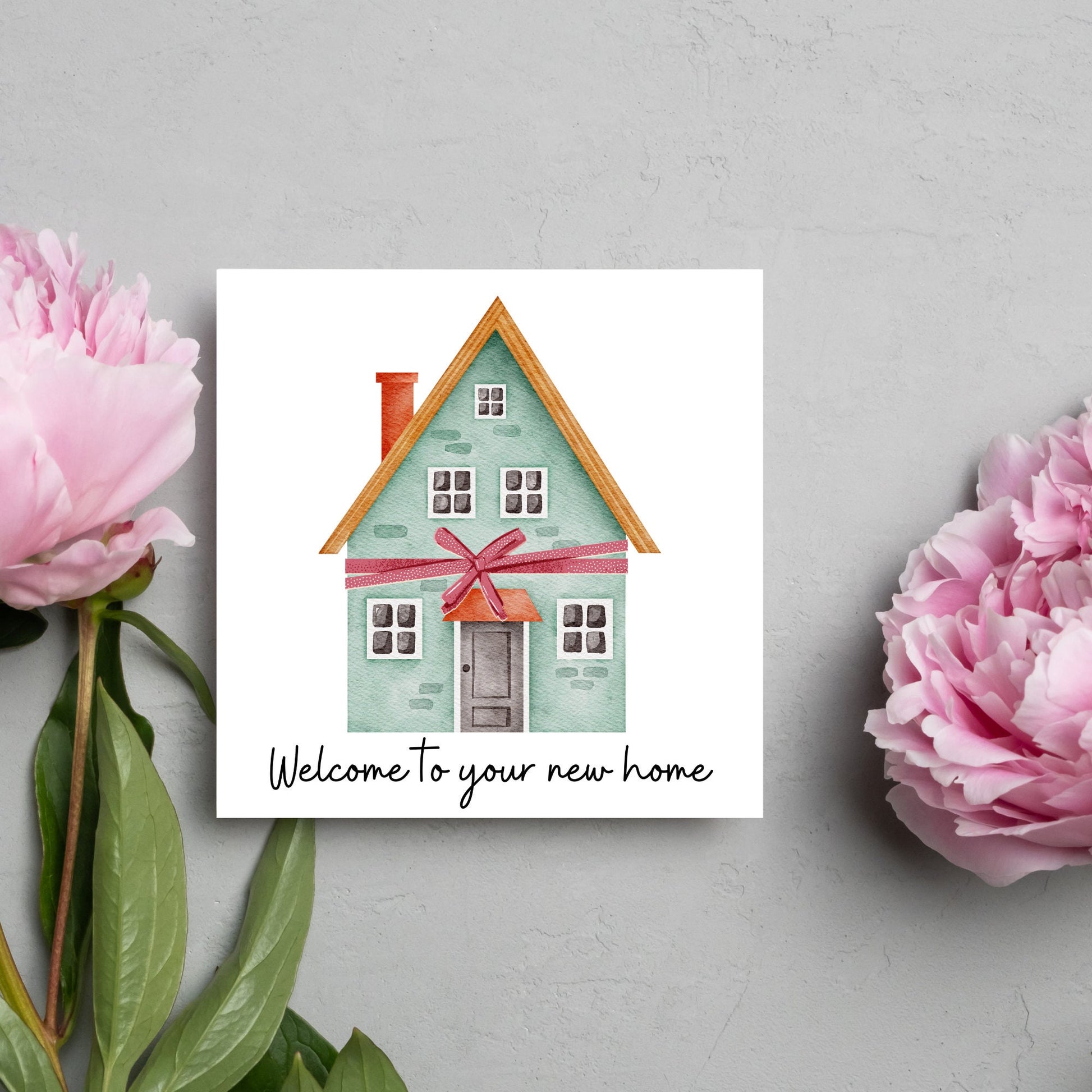 Square card with white background and a watercolour style illlustration of a green three storey house with a red bow wrapped around it. Underneath the house ina script font are the words 'welcome to your new home'