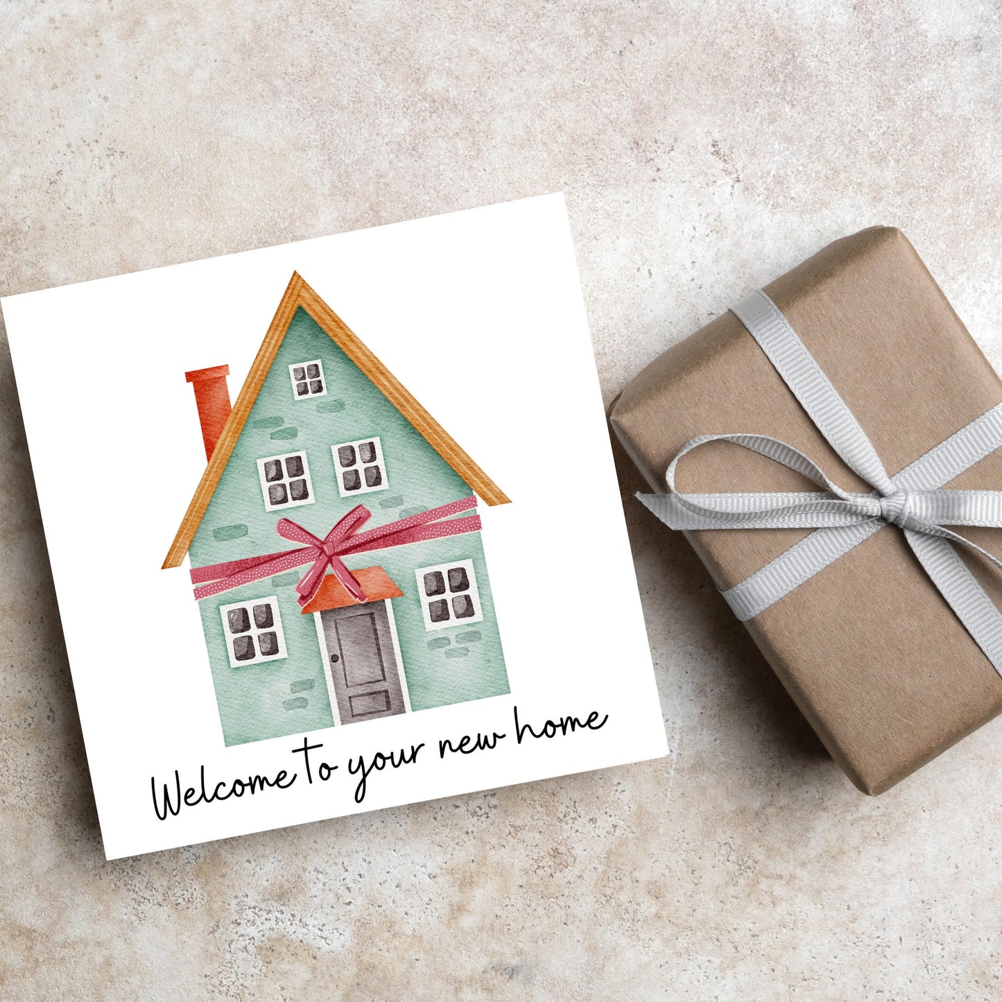 Square card with white background and a watercolour style illlustration of a green three storey house with a red bow wrapped around it. Underneath the house ina script font are the words 'welcome to your new home'