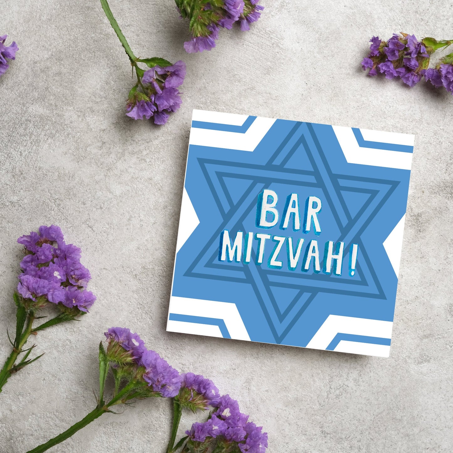 white and blue bar mitzvah card, geometric design with a repeating star of david at the centre in various shades of blue. At the centre of the card in white writing are the words 'bar mitzvah!' in capital letters in a handwritten style font