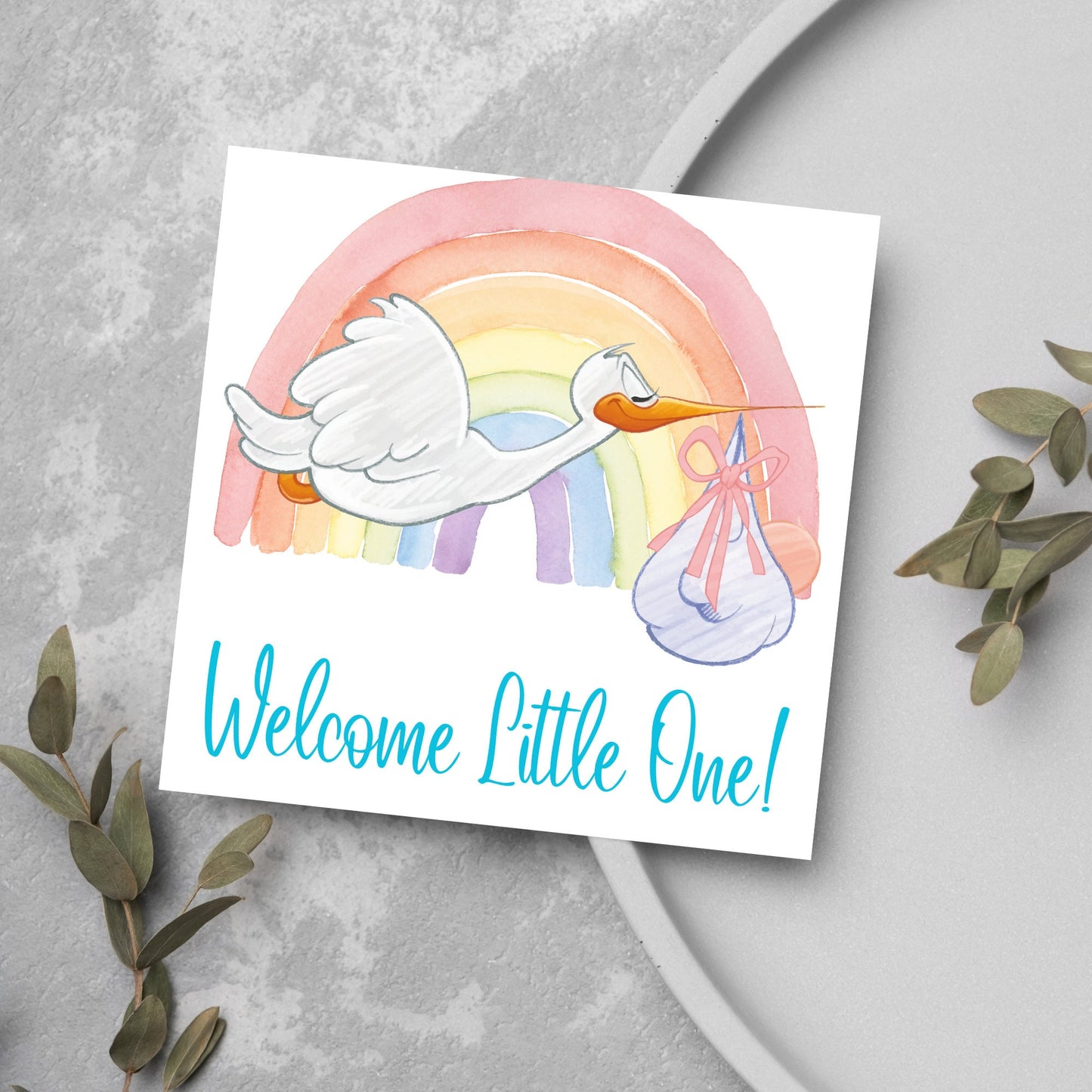 square new baby card with a flying cartoon stork delivering a swaddled baby against a watercolour rainbow in pastel shades. A cursive style text reads 'welcome little one' in a light blue font at the bottom of the card