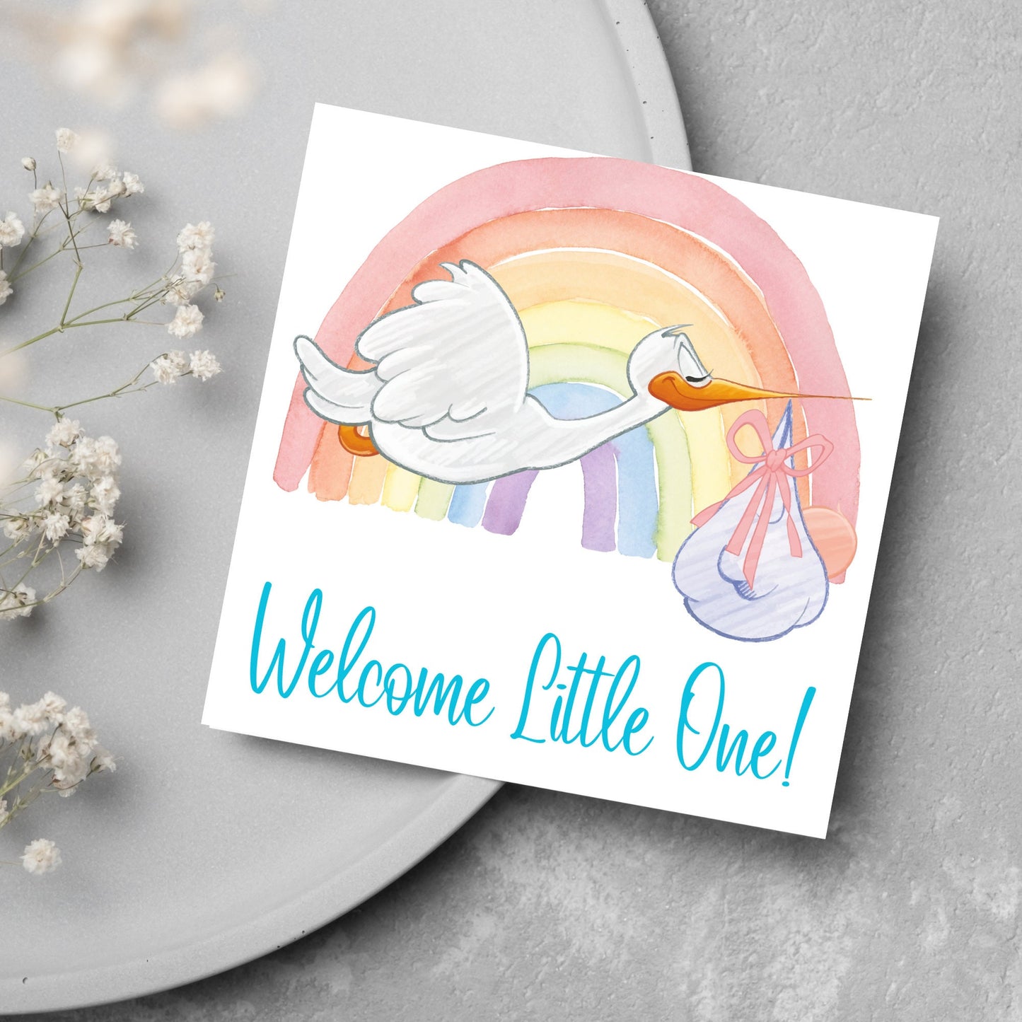 square new baby card with a flying cartoon stork delivering a swaddled baby against a watercolour rainbow in pastel shades. A cursive style text reads 'welcome little one' in a light blue font at the bottom of the card