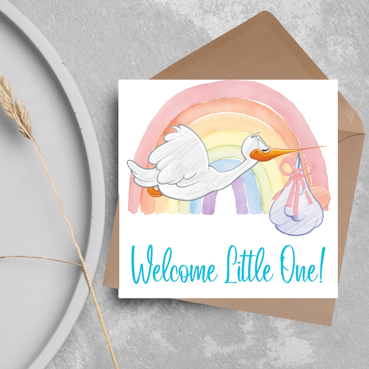 square new baby card with a flying cartoon stork delivering a swaddled baby against a watercolour rainbow in pastel shades. A cursive style text reads 'welcome little one' in a light blue font at the bottom of the card