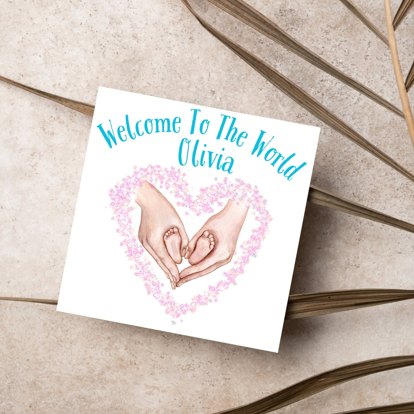 image of a square card with an illustration of hands holding newborn feet in a heart shape surrounded by pink flowers. Above the image is blue text that reads 'welcome to the world olivia' in a handwritten style font