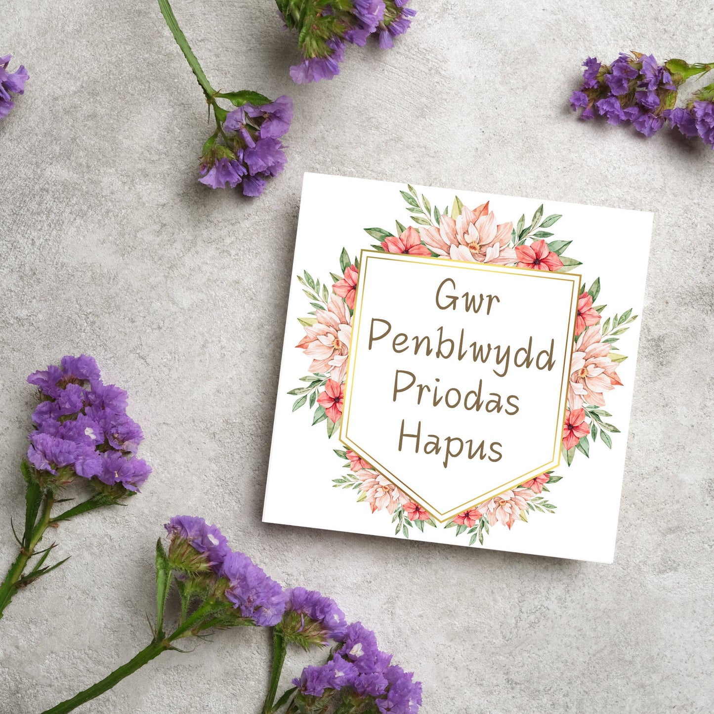 Image of a square wedding anniversary card with 'gwr penblwydd priodas hapus' in a subtle handwritten style font, which translates to 'happy wedding anniversary' in welsh. the text is against a white banner surrounded by pink flowers