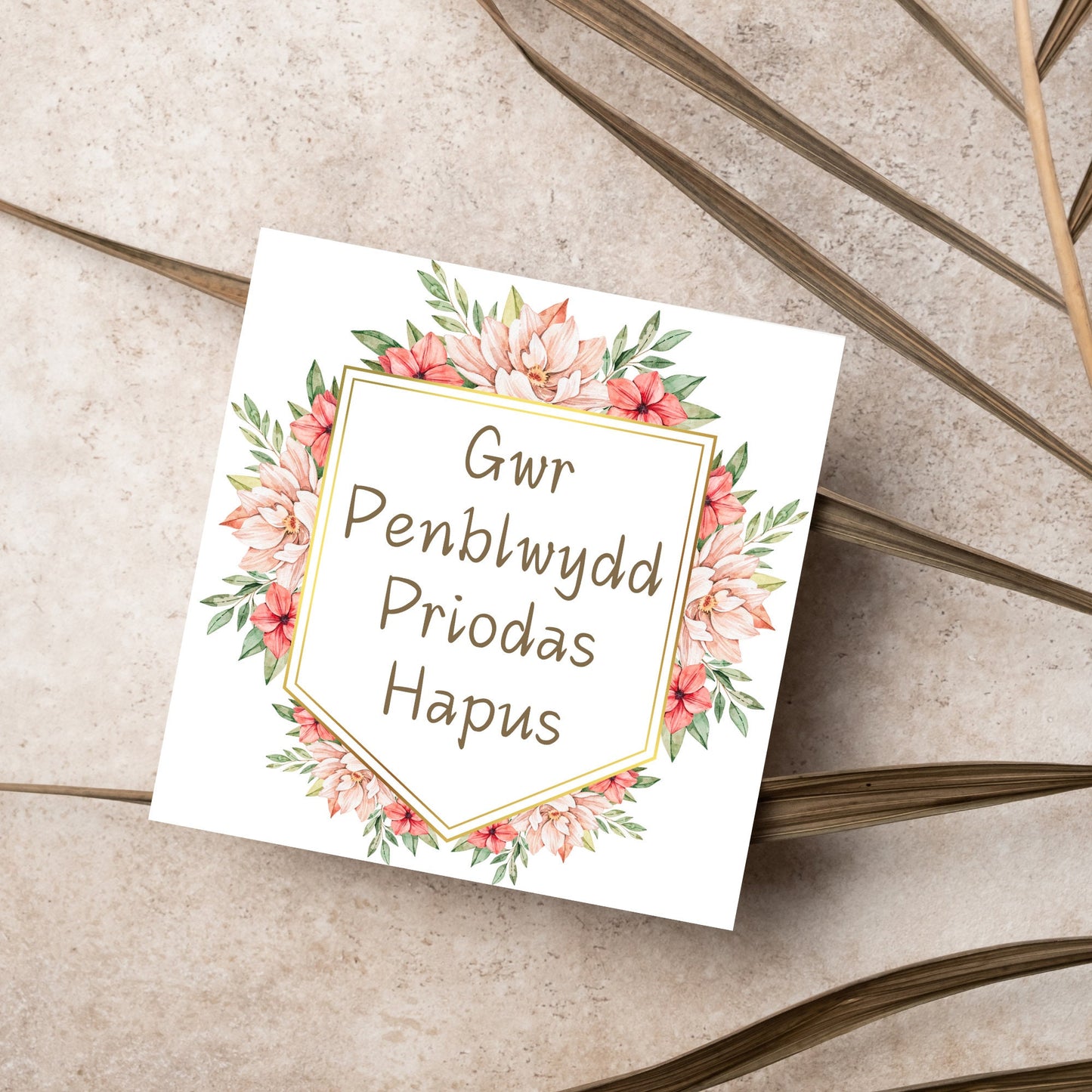 Image of a square wedding anniversary card with 'gwr penblwydd priodas hapus' in a subtle handwritten style font, which translates to 'happy wedding anniversary' in welsh. the text is against a white banner surrounded by pink flowers