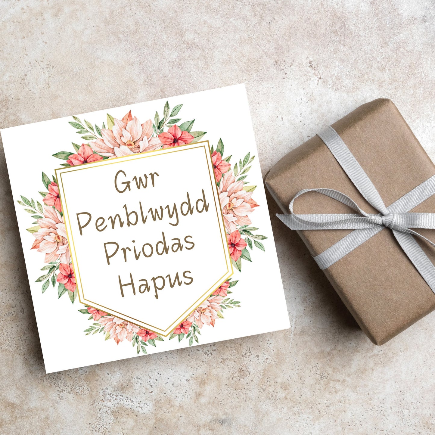 Image of a square wedding anniversary card with 'gwr penblwydd priodas hapus' in a subtle handwritten style font, which translates to 'happy wedding anniversary' in welsh. the text is against a white banner surrounded by pink flowers