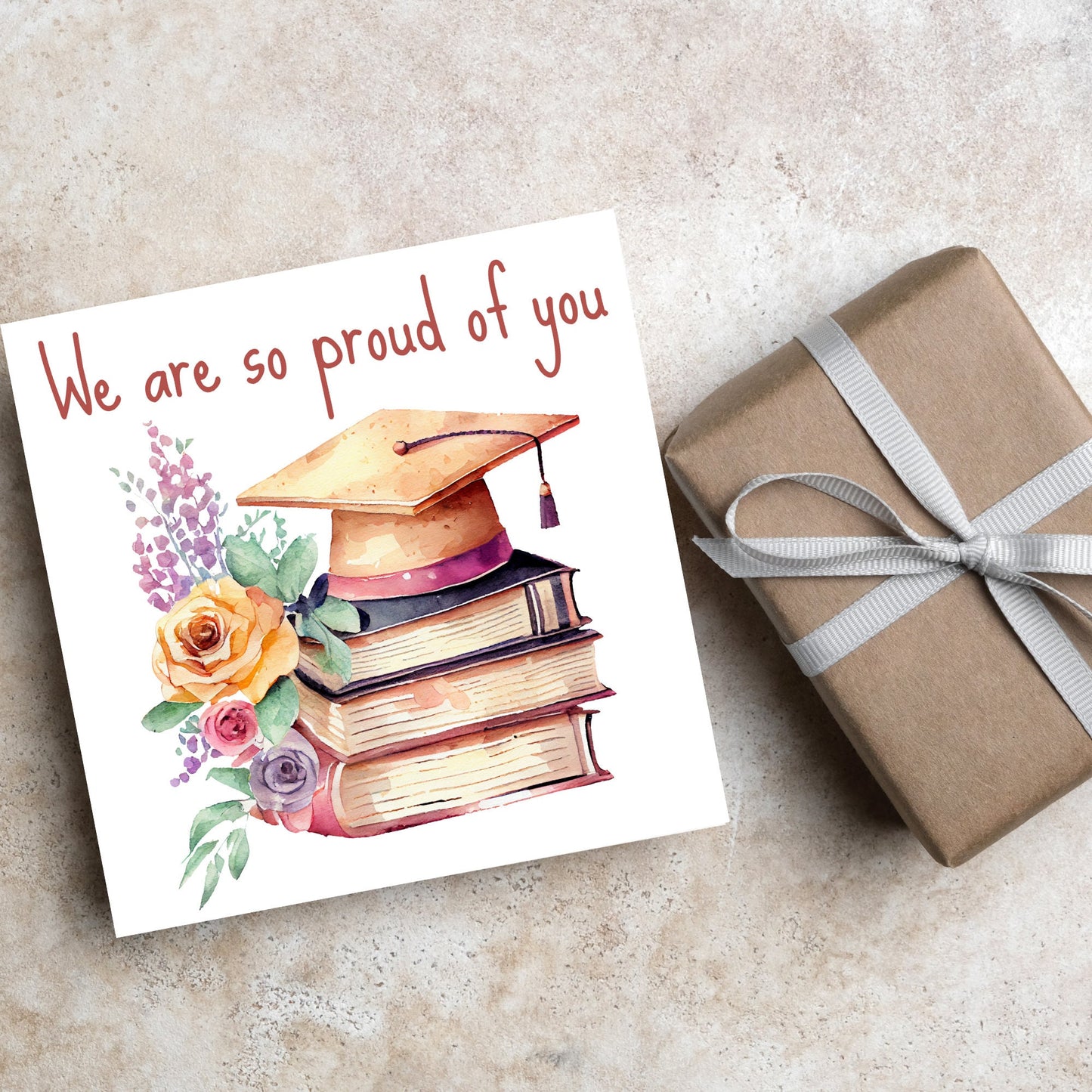 Image of a square graduation greeting card featuring a watercolour style image of a graduation cap on top of a stack of 3 books next to a floral arrangement. Above the image is the text 'we are so proud of you' in a handwritten font
